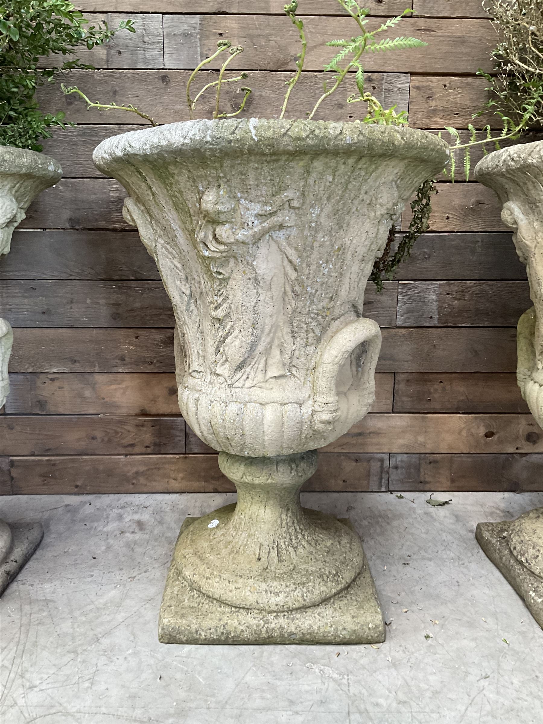Set of four Victorian design cast stone Grecian urns, tapering form cast with figures and handles, square plinth bases