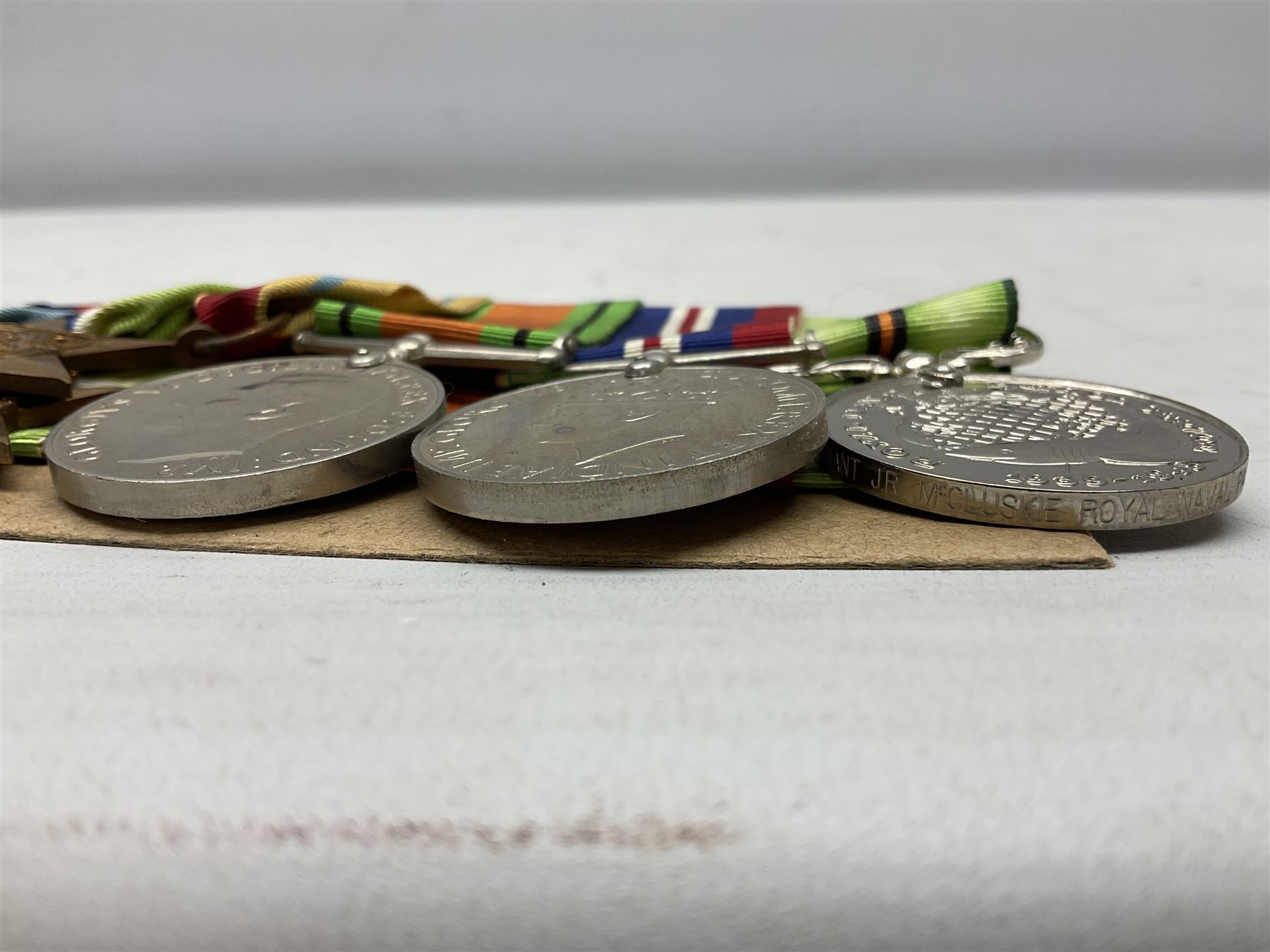 WW2 Royal Naval group of eight medals comprising OBE, hallmarked silver Distinguished Service Cross inscribed verso Lieut. J.R. McCluskie RNVR 1945, 1939-1945 Star, Atlantic Star, Africa Star, 1939-1945 War Medal, Defence Medal and Royal Naval Patrol Service Medal inscribed Lieutenant J.R. McCluskie Royal Naval Patrol Service; with seven original photographs of a sea battle 27th November 1940 against the Italian Fleet and another photographic postcard of Sir Stafford Cripps arriving on board one of the vessels.