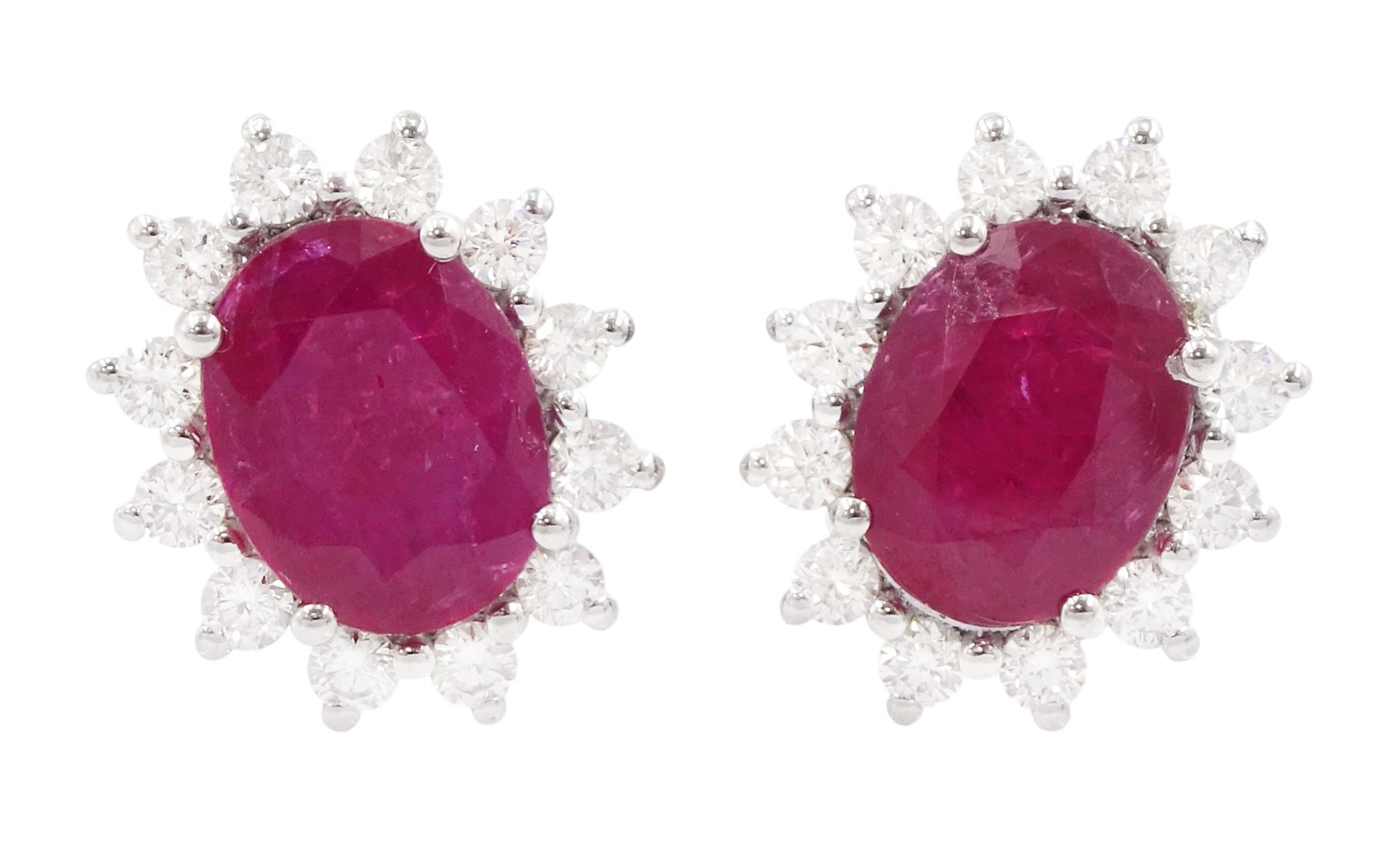 Pair of 18ct white gold ruby and diamond earrings, each stud set with a single oval cut ruby, surrounded by twelve round brilliant cut diamonds, stamped, total ruby weight approx 3.10 carat, total diamond weight approx 0.50 carat