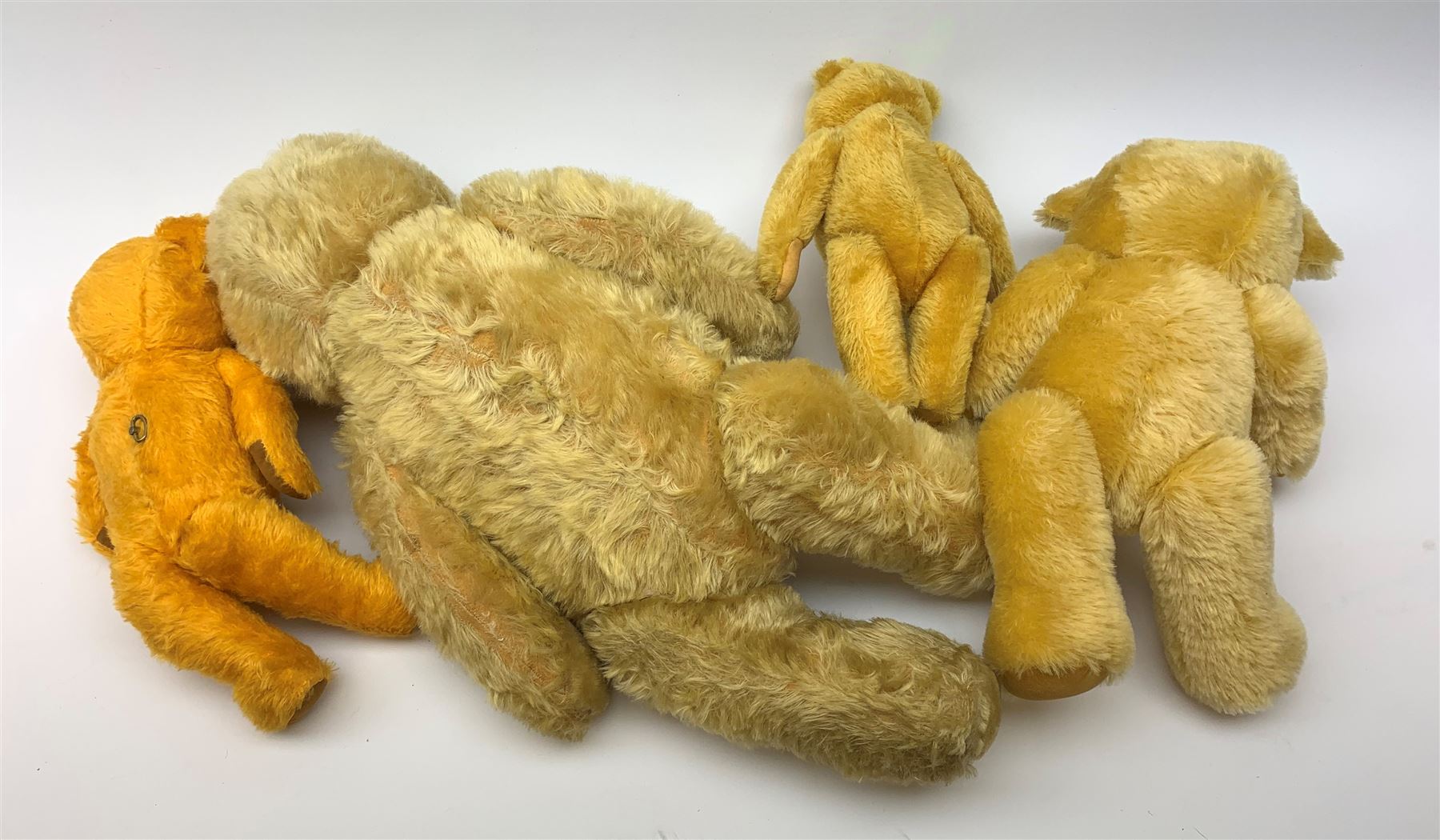 Four 1950s English/European teddy bears including an orange plush wind-up musical bear with swivel jointed head, glass type eyes, vertically stitched nose and mouth and jointed limbs with felt paw pads H19