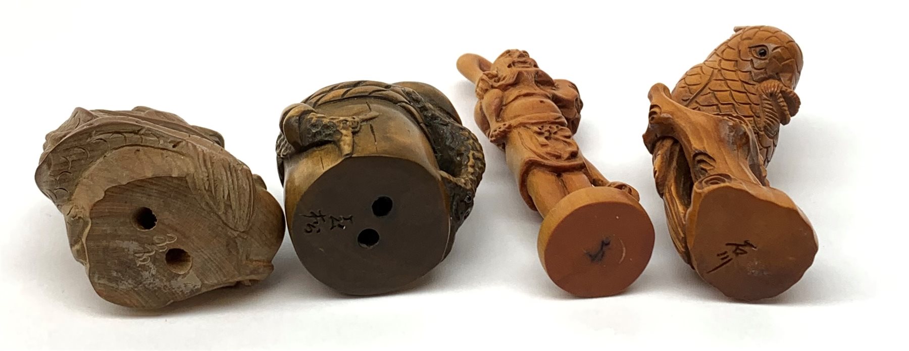Four carved wooden Japanese netsukes, modelled as a dragon, two snails upon a log, a bird perched upon a branch, and a fisherman with figure upon his back, each signed beneath. (4). 