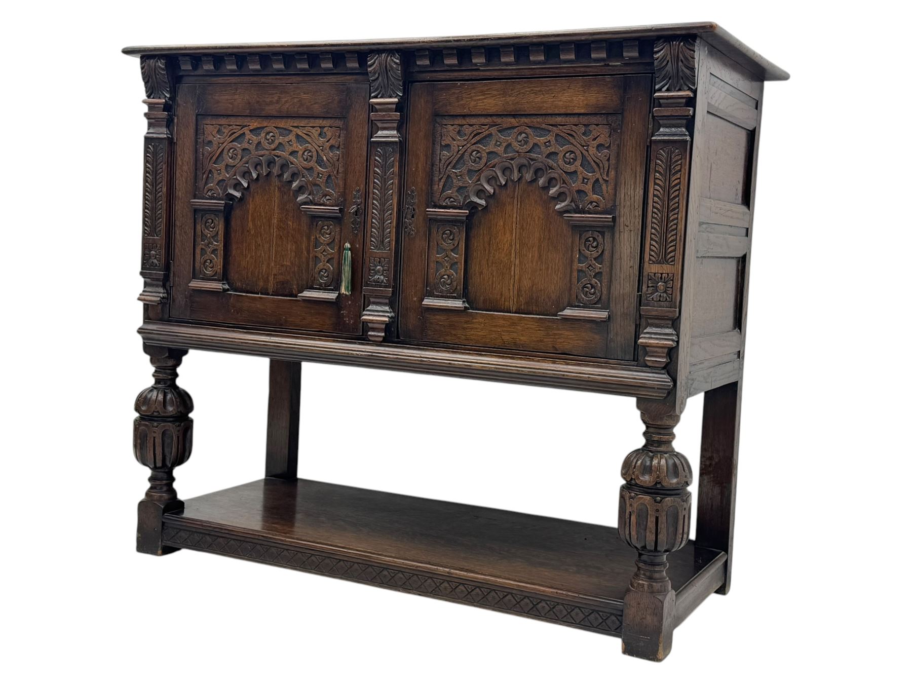 Jacobean design carved oak two door cupboard, the frieze and twin cupboard doors carved with arcaded panels and stylised foliage, raised on baluster supports united by an undertier