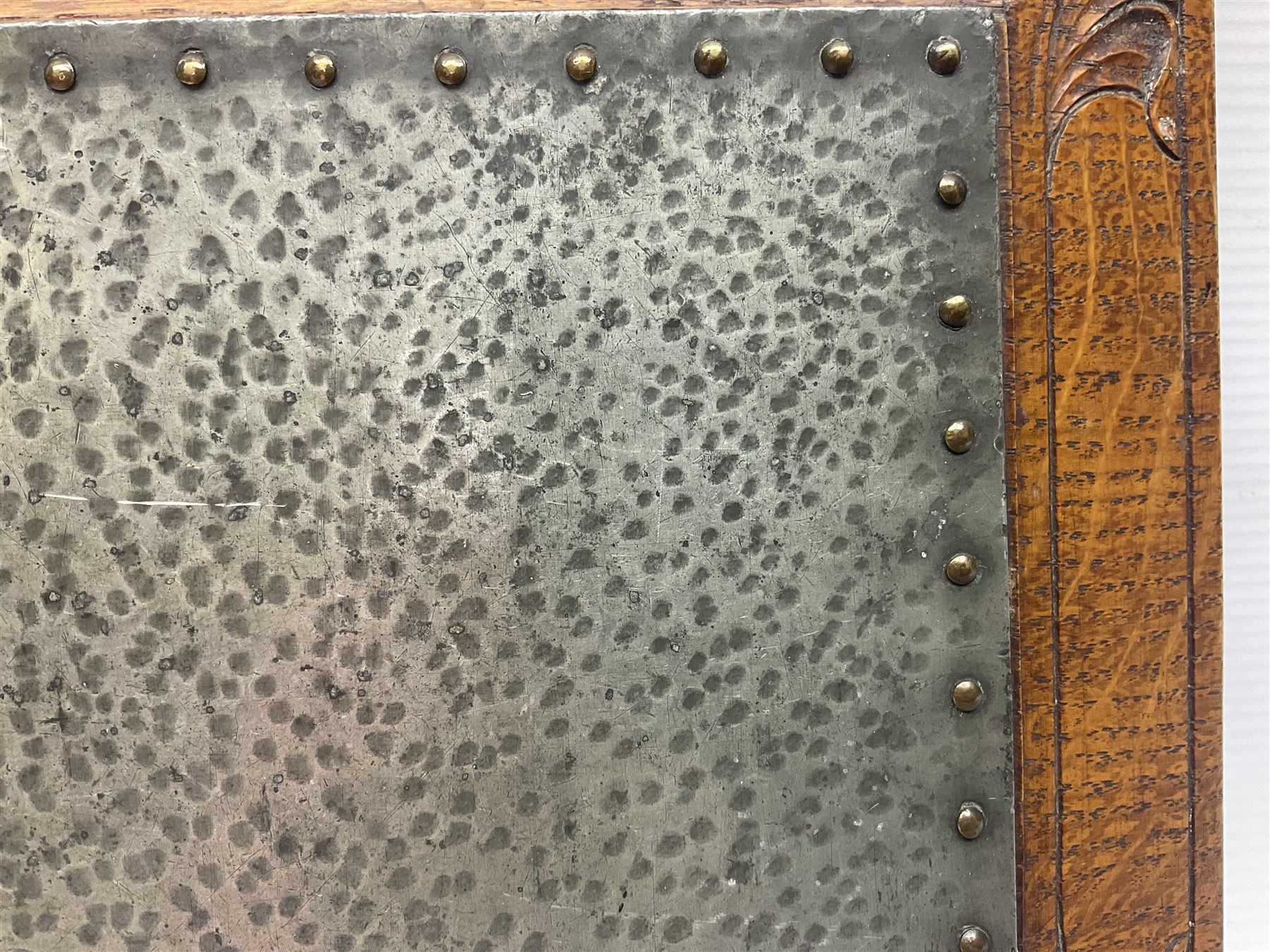 Arts and Crafts oak stand by Arthur Simpson of Kendal, of rectangular form with central hammered pewter panel, surrounded by a border with carved foliate corners, upon two bar supports, bearing label detailed 