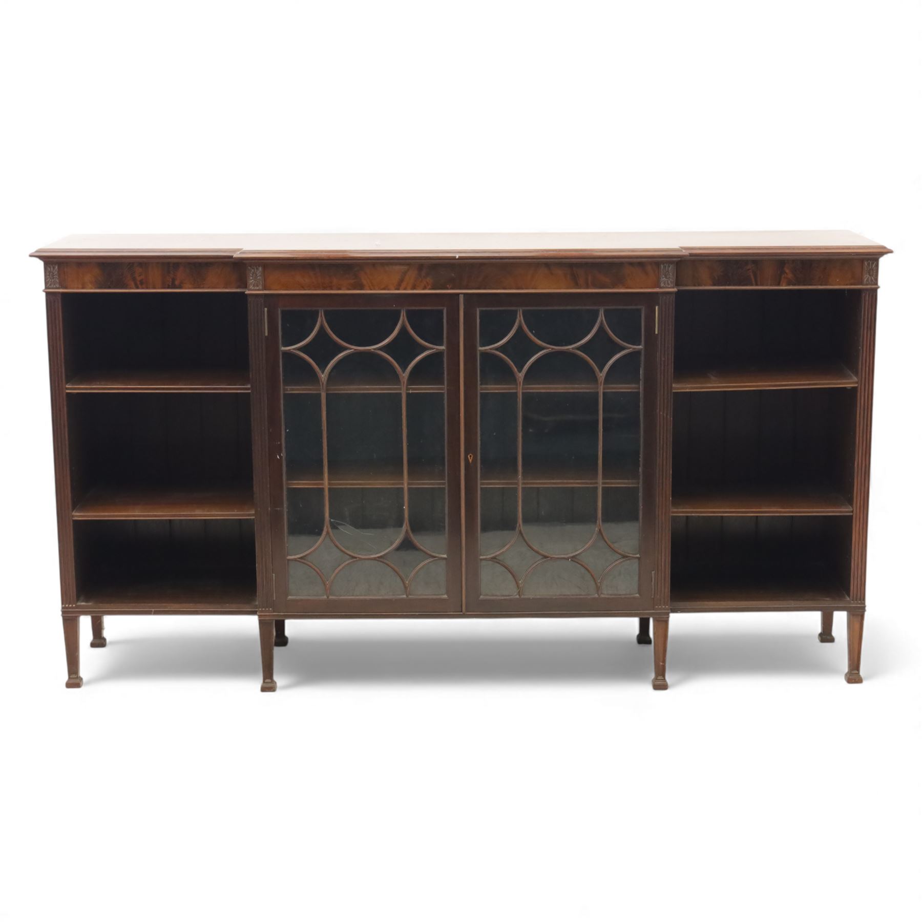 Early 20th century mahogany breakfront bookcase cabinet, the moulded rectangular top above a central pair of astragal glazed doors with arched glazing bars enclosing shelving, flanked by open book shelves, raised on square tapering supports with block feet