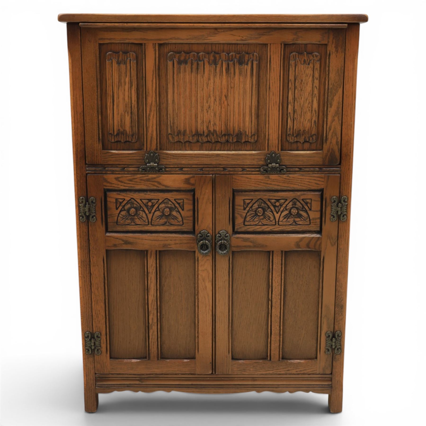 Old Charm - carved oak bar with three bar stools and associated Old Charm drinks cabinet, carved top with channels for glassware beneath, bar surface above glazed panels, shelves for glassware to the back, associated Old Charm drinks cabinet with fall front linenfold carving, above twin doors with shelved interior