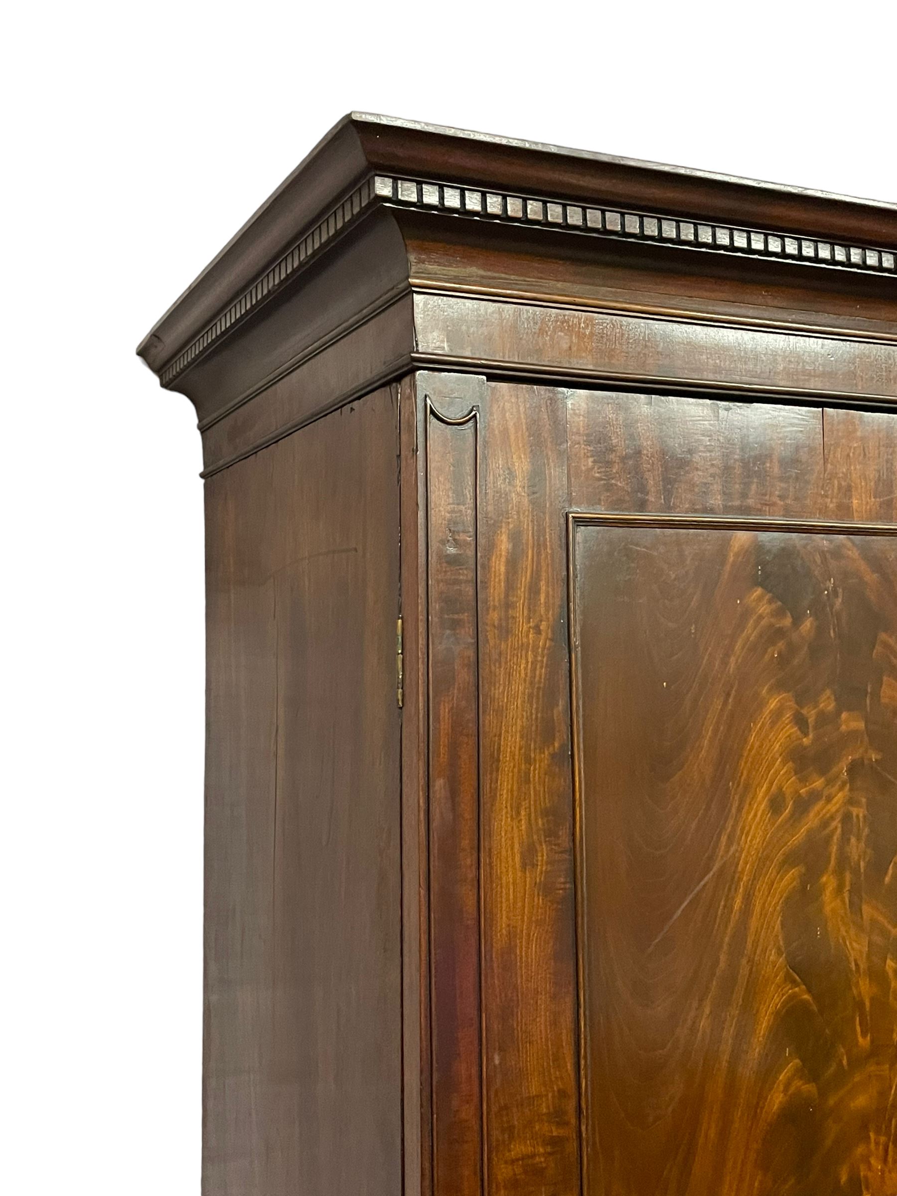 George III mahogany double wardrobe, the projecting cornice with dentil moulding over two panelled doors with mirror-lined interiors, enclosing hanging rails and brass hooks, the base fitted with two drawers, raised on bracket feet