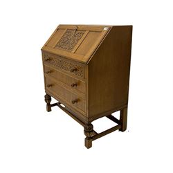 Early 20th century golden oak bureau, panelled fall front carved with scrolling foliage enclosing fitted interior, above three long drawers, the top drawer front with blind fretwork decoration