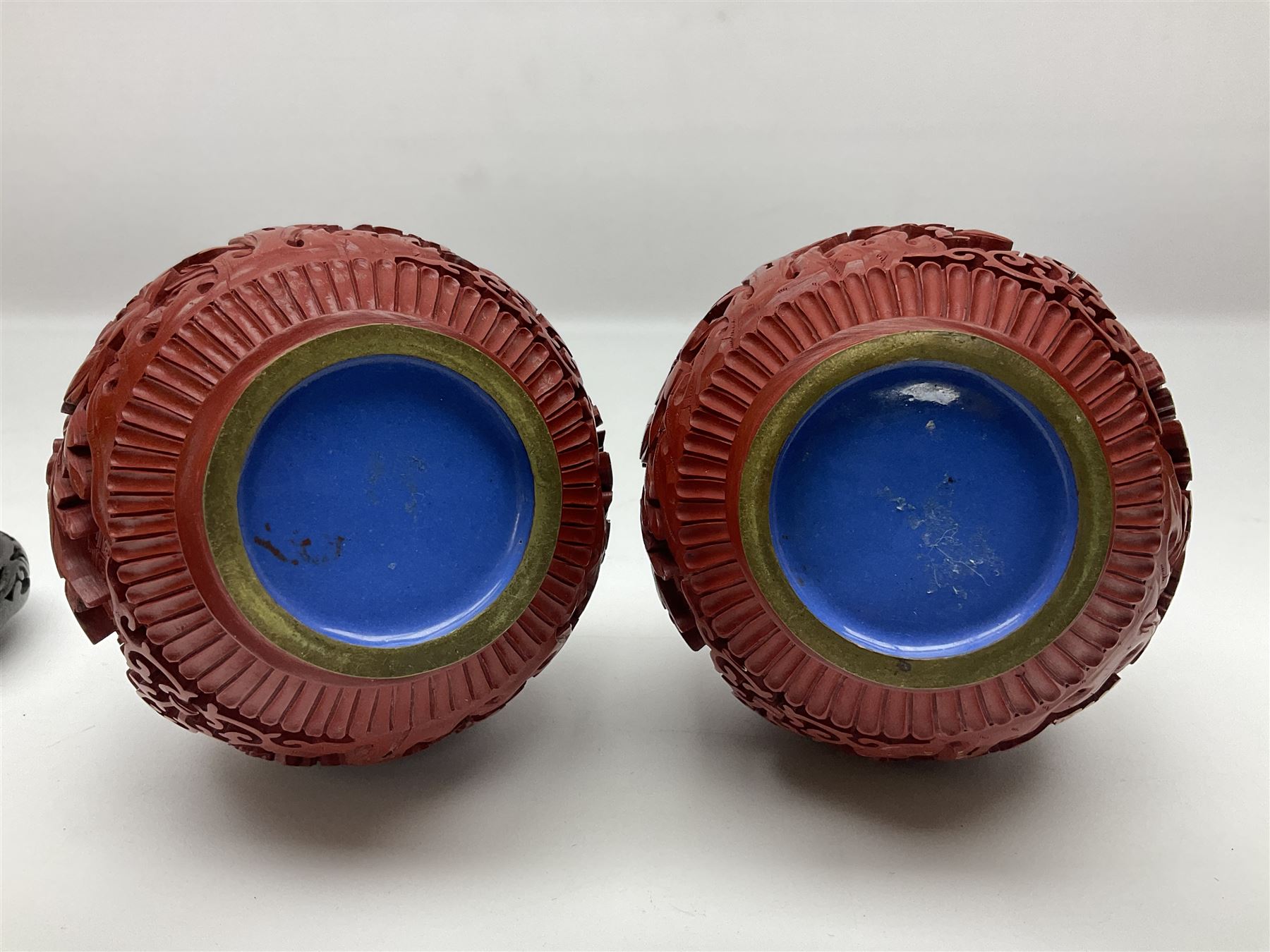 Pair of Chinese cinnabar lacquer vases, each of bulbous baluster form, carved with peonies and foo dogs amongst scrolls, with blue enamel interior and upon wooden bases, H20cm