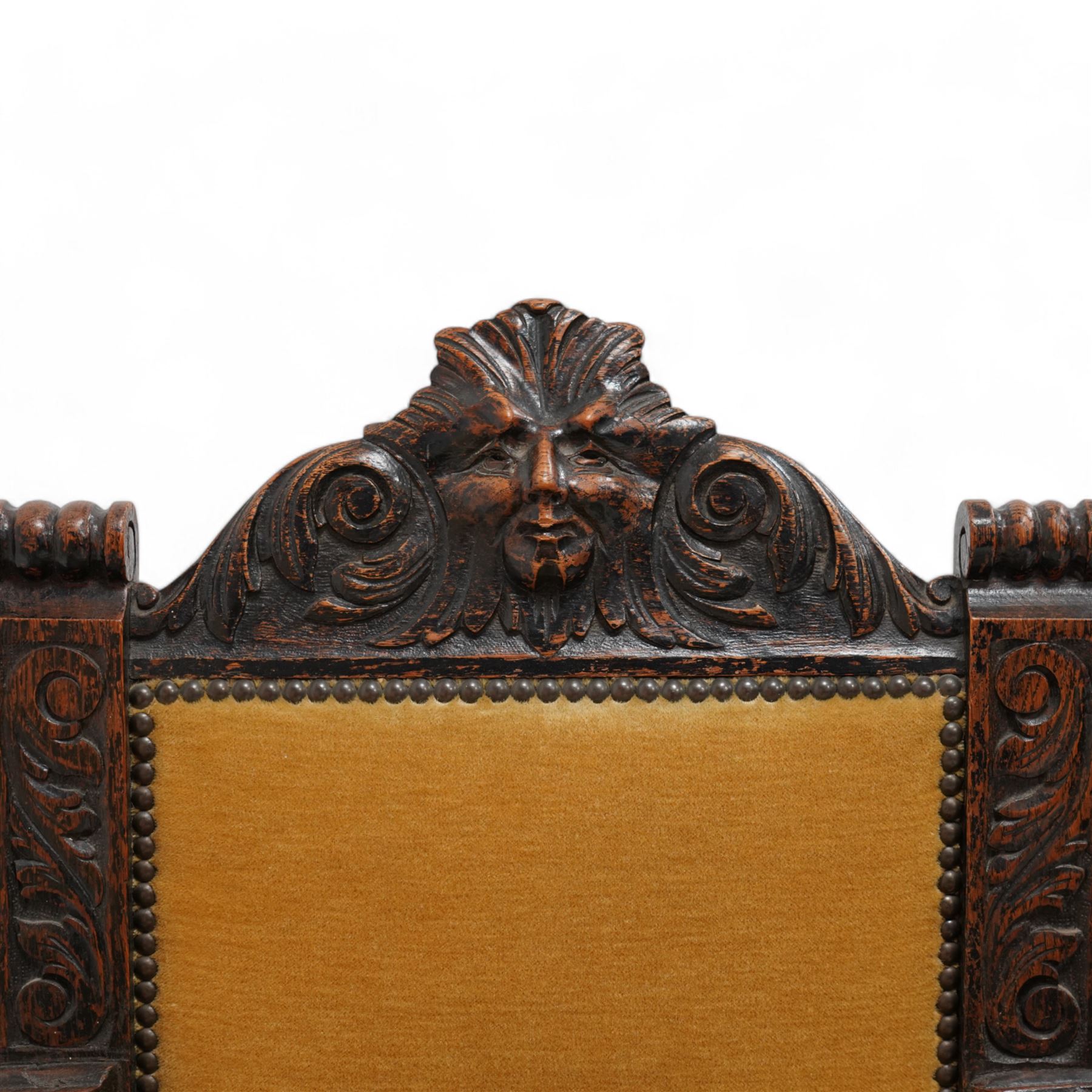 Victorian heavily carved oak X-framed throne chair, the cresting rail carved with mask and curling foliage, upholstered in mustard fabric, the arms and frame carved with scrolling foliage, united by turned stretchers 