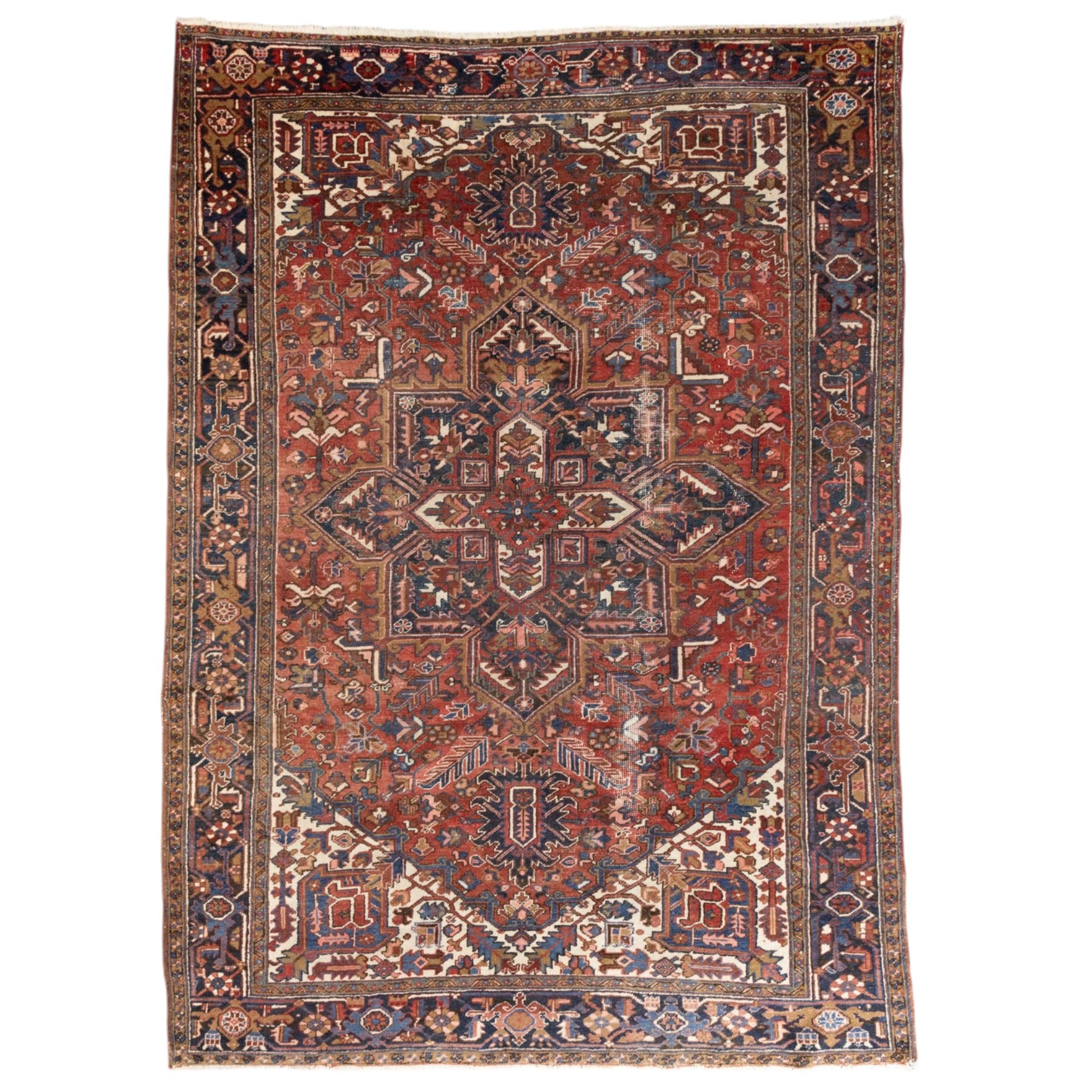 Persian Heriz carpet, red ground with large central geometric medallion, angular flowering branches and stylised foliate decoration, within a broad dark blue floral border and narrow guard stripes