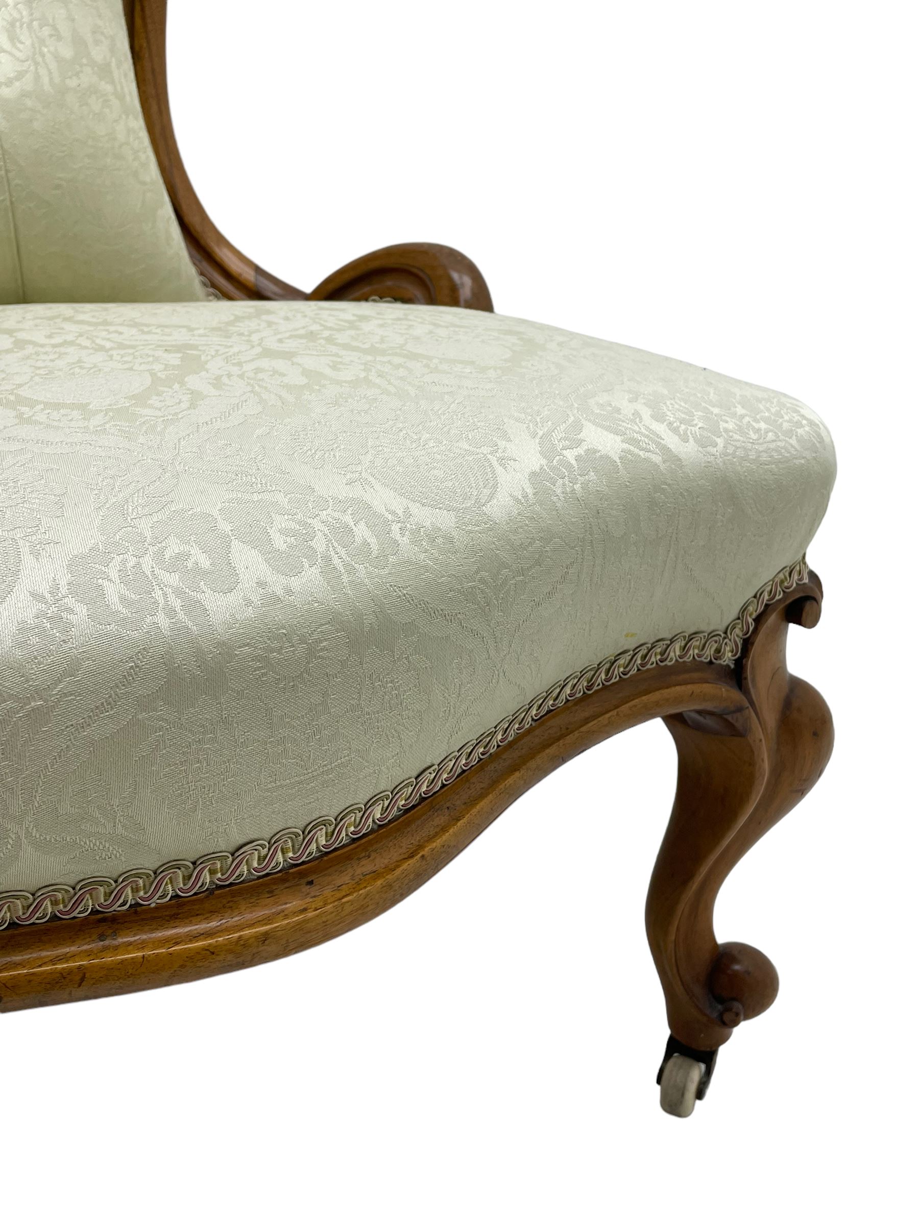 Victorian walnut framed nursing chair, the cresting rail decorated with carved applied flower heads and acanthus leaves, shaped back and sprung seat upholstered in buttoned ivory damask fabric, serpentine front over cartouche carved cabriole supports with ceramic castors (W57cm H92cm); with matched footstool, circular top over shaped moulded apron, on floral carved cabriole feet (W34cm) 