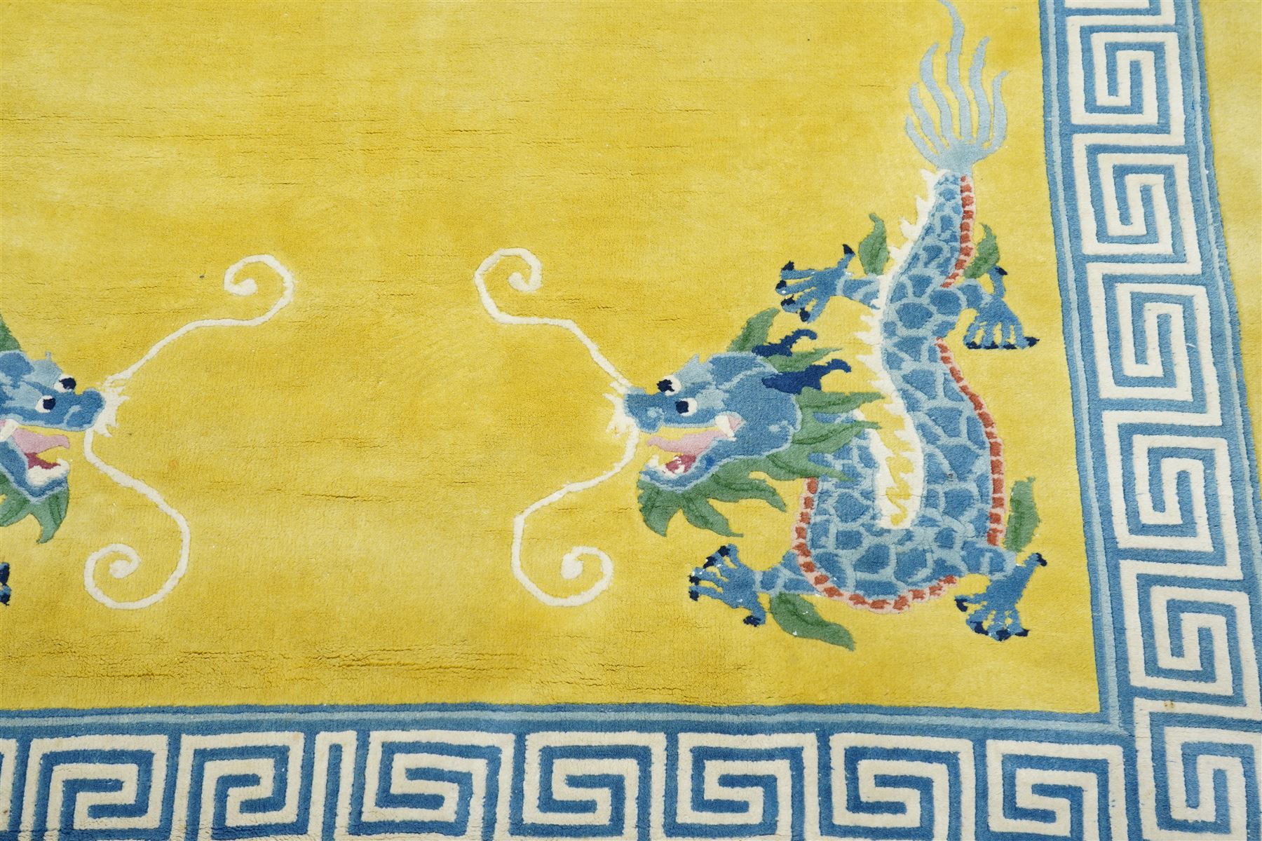 Modern Chinese hand-knotted wool pile carpet, golden field decorated with conforming dragons amidst stylized cloud scrolls enclosed by a Greek gey meander border, with cotton fringe ends 