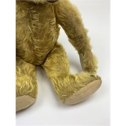 Early 20th century German teddy bear c1920, probably Steiff or Bing, with wood wool filled humped back golden mohair body, swivel jointed head with glass eyes and brown vertically stitched nose and mouth, jointed limbs with elongated arms and felt paw pads with black stitched claws H18