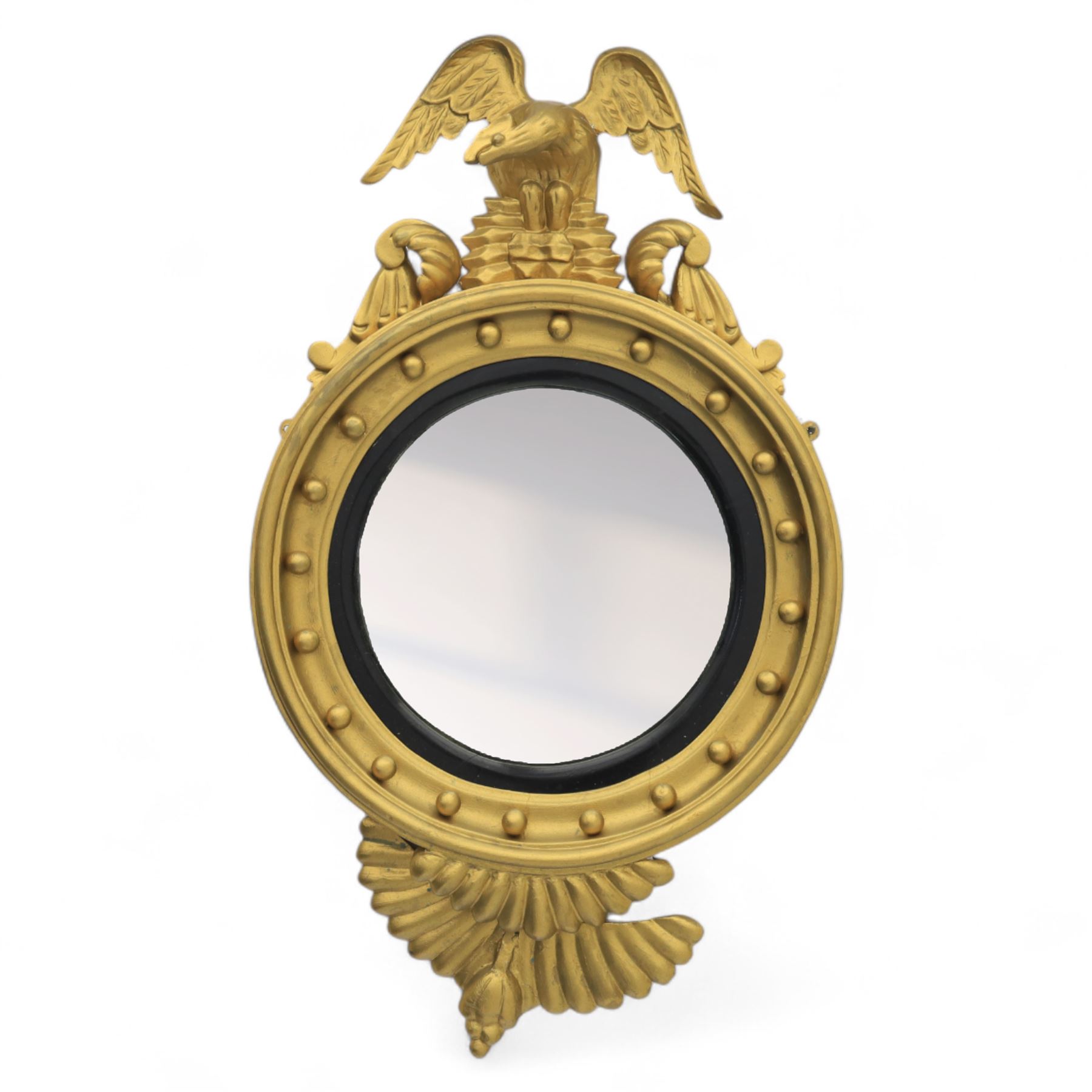 Early 20th-century Regency-style giltwood convex mirror, circular plate within a ball-mounted frame surmounted by an eagle cresting and flanked with scrolls, apron carved with foliate decoration 