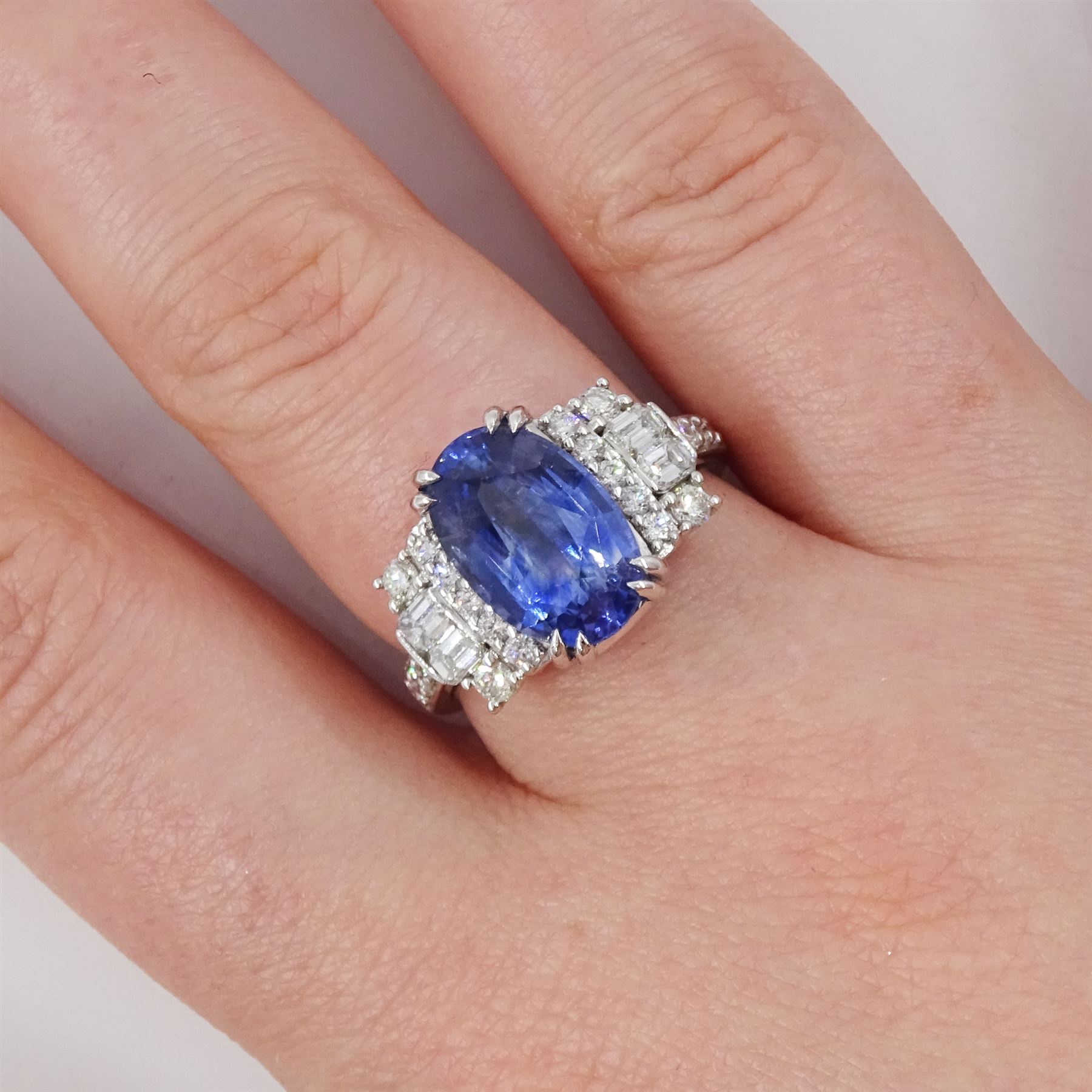 18ct white gold Ceylon sapphire and diamond dress ring, single oval cut sapphire of 4.65 carat, either side set with round brilliant cut and baguette cut diamonds and diamond set shoulders, stamped 750, total diamond weight 0.77 carat, with World Gemological Institute report