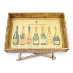 Champagne butler’s tray on stand, the wooden tray printed with champagne bottles and brand names, with cutout handles, raised on a folding stand