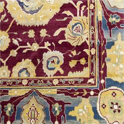 Agra design wool carpet, burgundy field decorated with large scrolling floral vines, palmettes and flowerheads, enclosed by blue main border with oversized stylised palmettes and narrow guard stripes