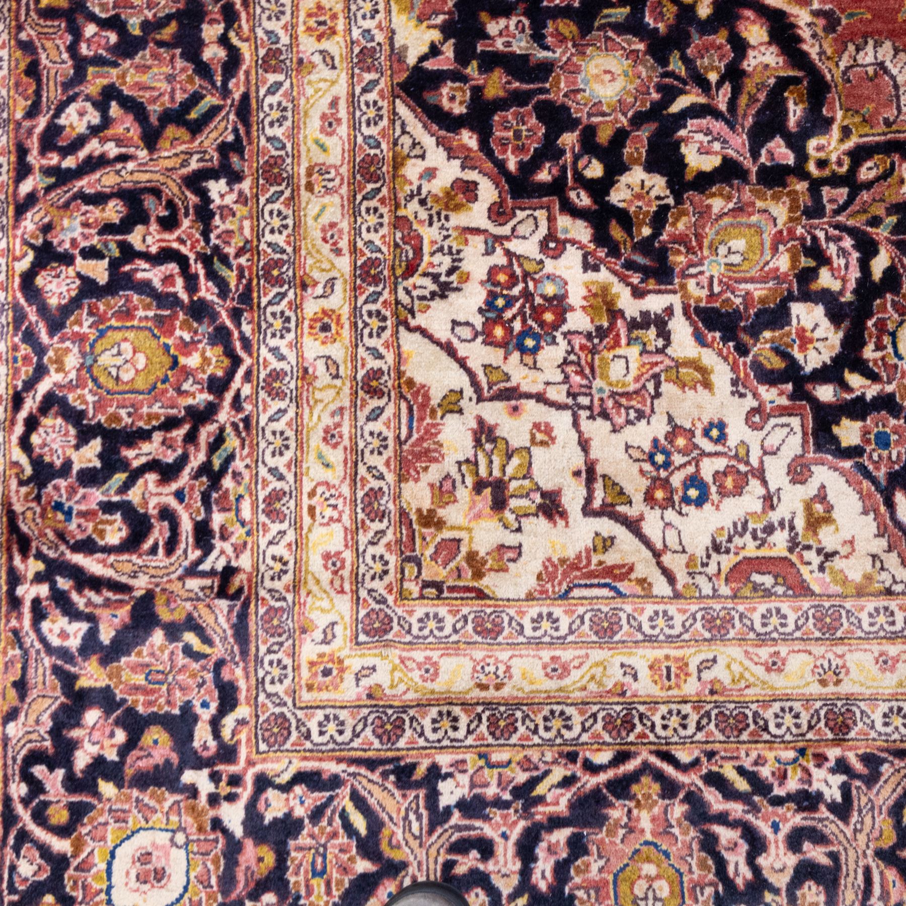 Large Central Persian Kashan hand-knotted carpet, madder red field with central cusped medallion on beige ground enclosed by indigo border with an intricate all-over arrangement of scrolling vines and floral motifs within conforming spandrels and a indigo ground main border ornamented with floral designs, enclosed by guard stripes and cotton fringe ends 
