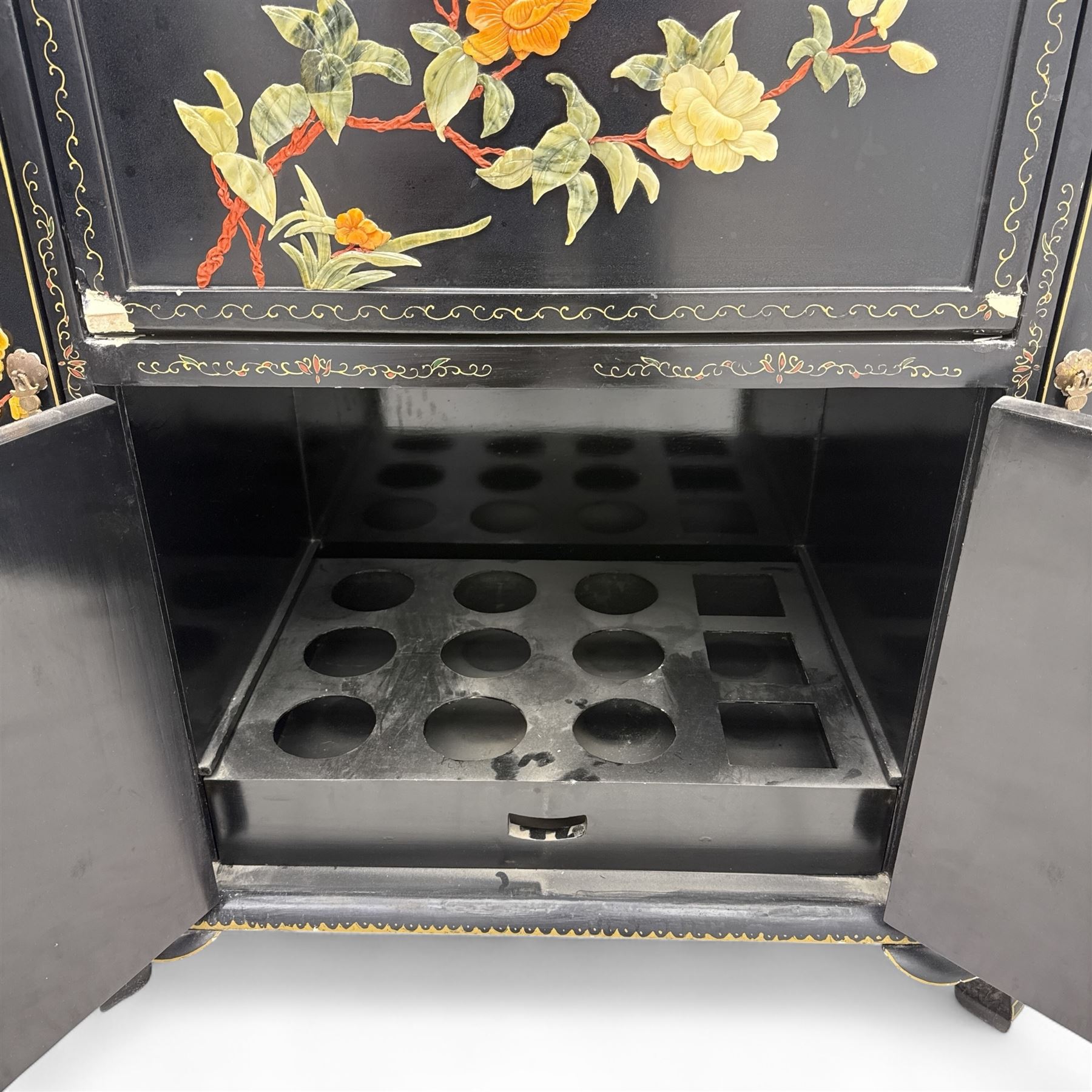 Early 20th century Chinoiserie lacquered cabinet, rounded rectangular top above a fall front enclosing fitted interior with lacquered decoration, over a pair of cupboard doors and flanked by side compartments with tiered bottle shelves, the black lacquer ground decorated throughout with raised and painted floral sprays, on shaped bracket feet