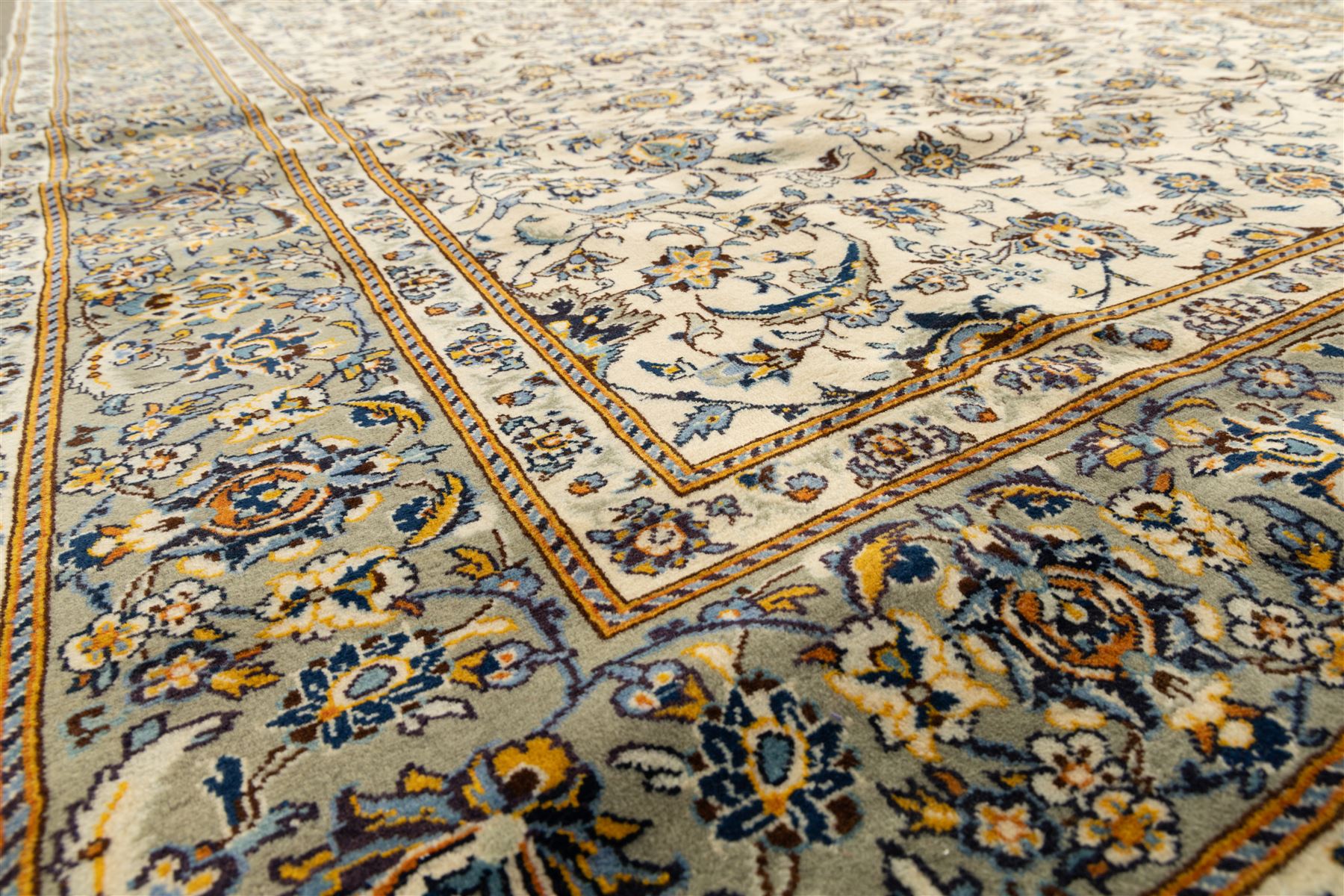 Central Persian Kashan hand-knotted rug, ivory field intricately decorated with an all-over design of scrolling vines, palmettes, and stylized lotus motifs in shades of soft blue, pale gold, and indigo within floral borders