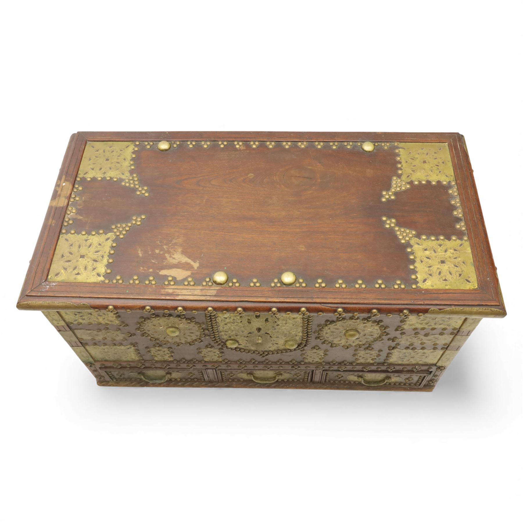 Early 20th century brass-mounted hardwood chest, the hinged top and front richly decorated with applied and studded brass panels and pierced lock escutcheon, revealing a candle box, reinforced with brass corner mounts