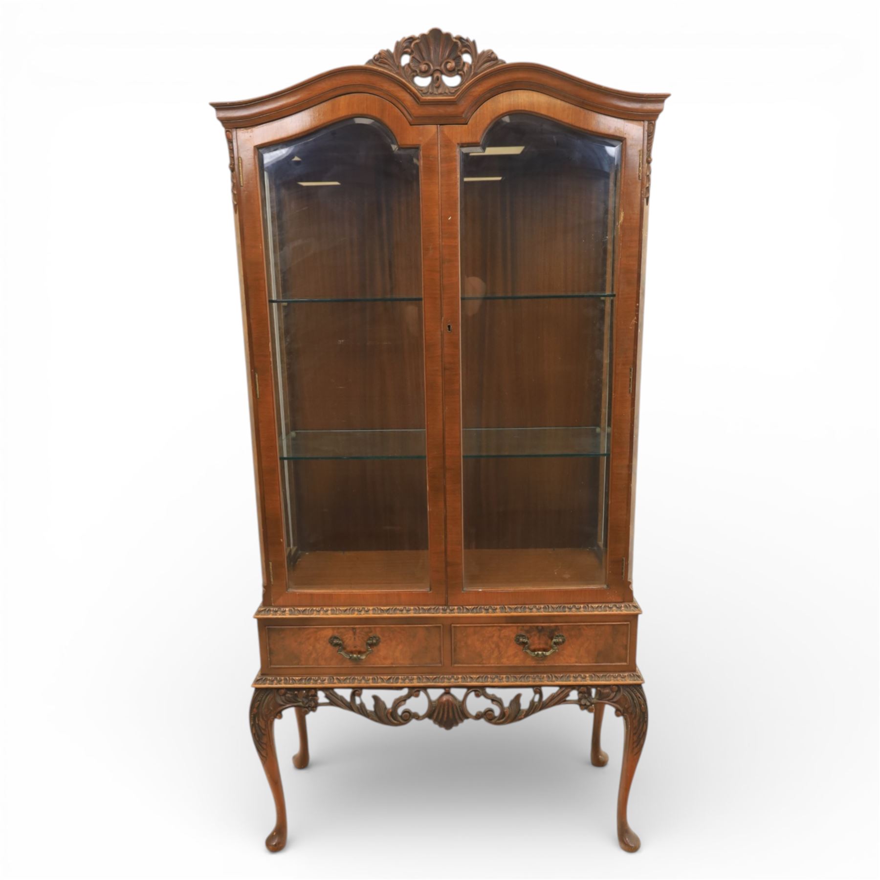 Queen Anne design walnut display cabinet, carved cartouche above two glazed doors enclosing two fixed glass shelves, over two frieze drawers above a heavily carved apron with cabriole supports