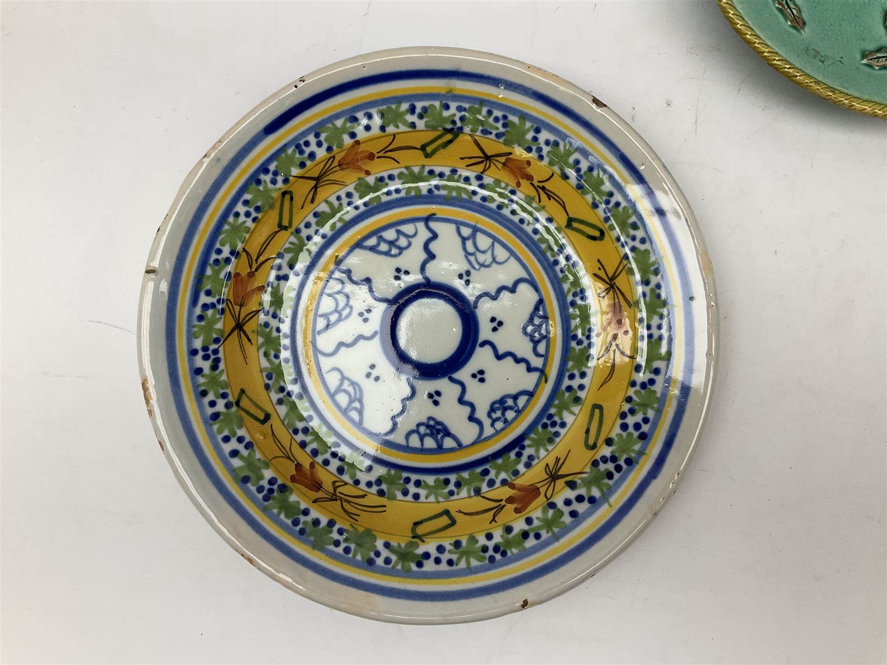Majolica plate decorated with yellow and brown bird upon fruiting holly branches on teal ground with mustard rope twist border, together with two other plates to include a Faience style example, D27cm
