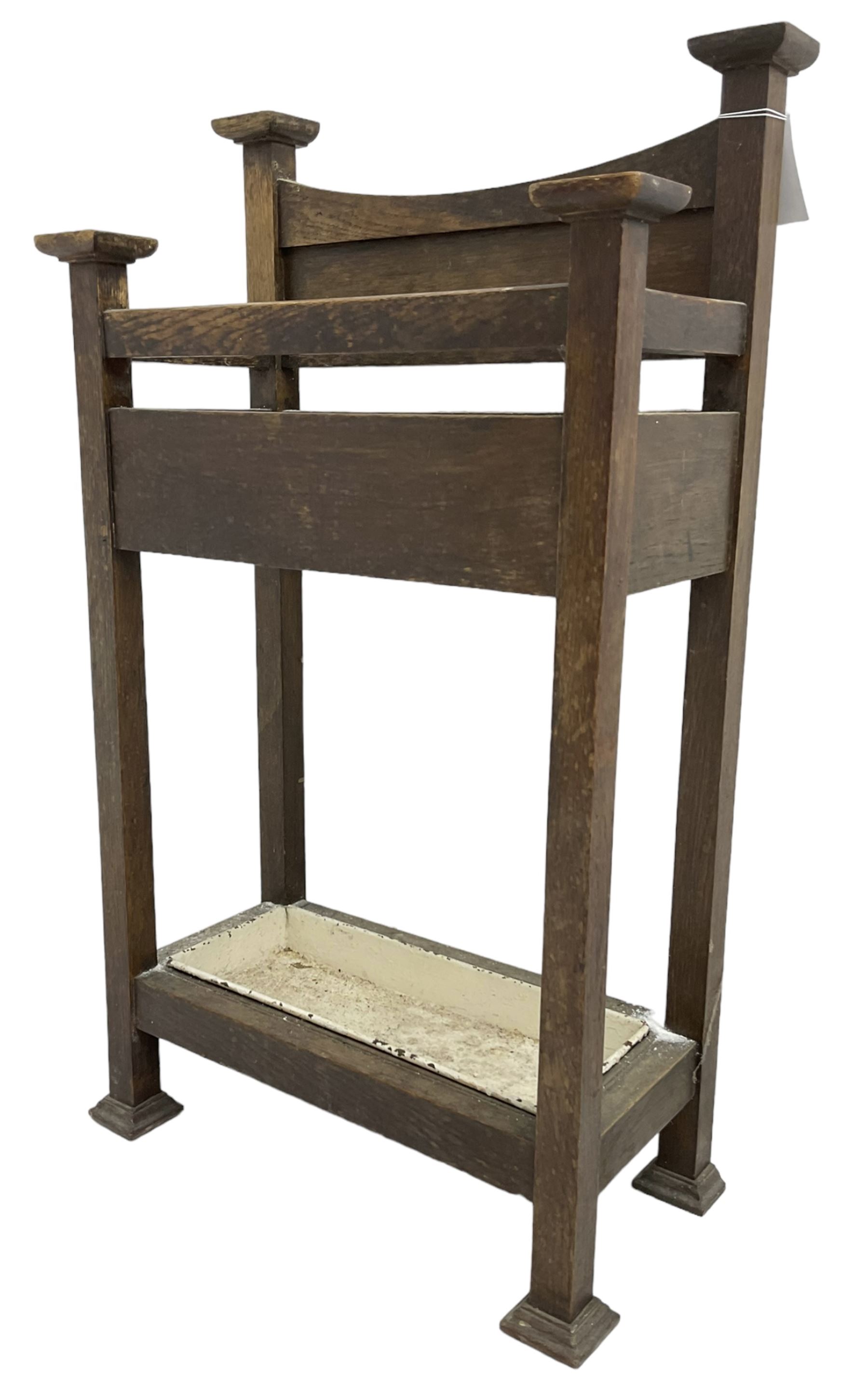 Early 20th century Arts & Crafts oak stick stand, panelled back over three divisions, fitted with metal drip tray, on square supports