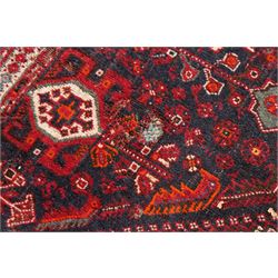 Large Persian Shiraz crimson ground carpet, the busy field decorated with a geometric pole medallion surrounded by stylised plant motifs with contrasting indigo spandrels and geometric-woven guard bands
