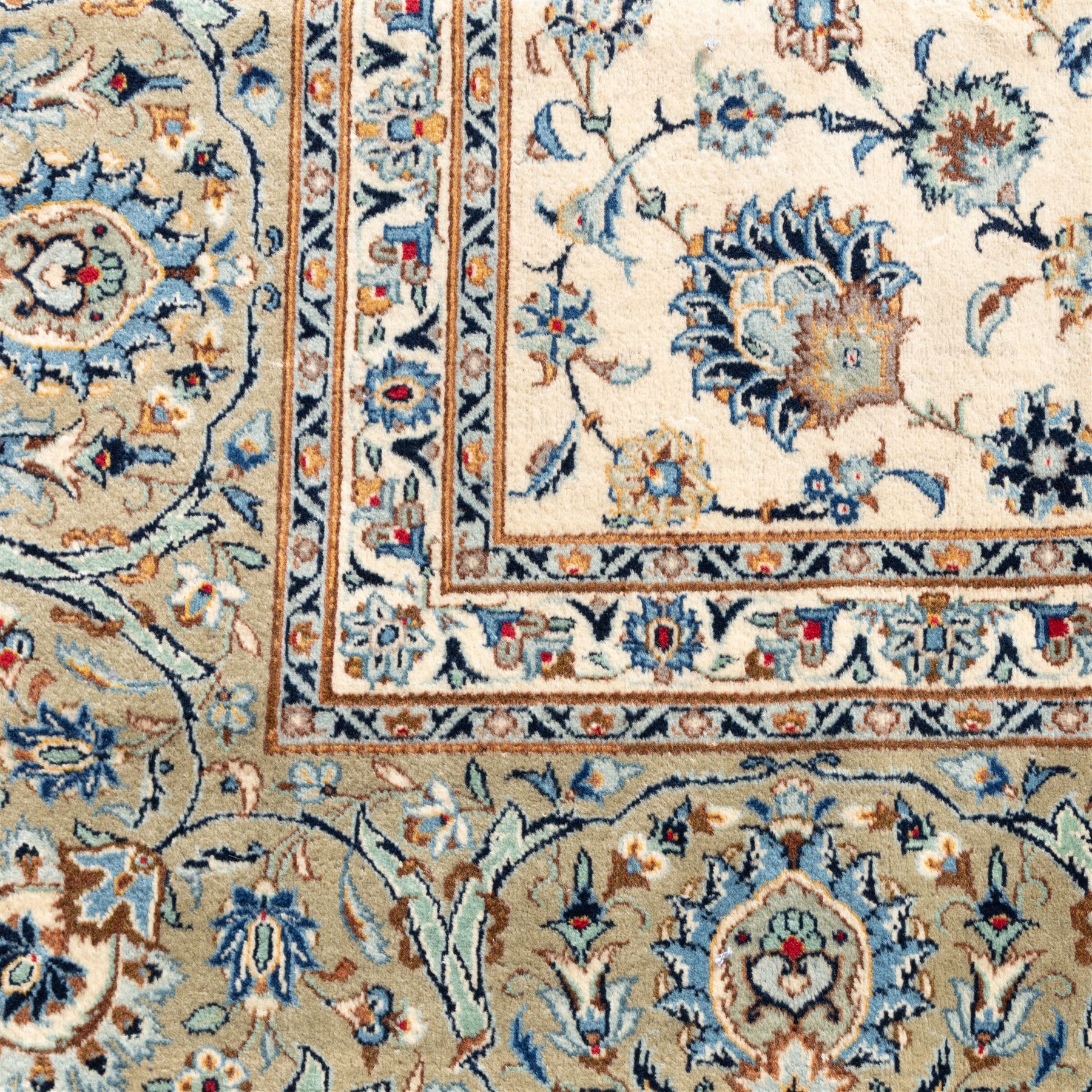 Large Central Persian Kashan hand-knotted carpet, ivory field with small central floral medallion issuing an all-over design of palmettes, rosettes, and scrolling vines enclosed by a complimentary foliate border framed by guard stripes, in a palette of ivory, power blues, and muted polychrome tones, with cotton fringe ends 