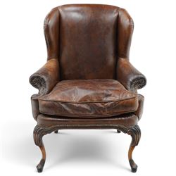 Pair of quality Queen Anne design mahogany framed wingback armchairs with matching footstools, the high sprung winged backs over rolled arms with studwork, raised on elegant reeded scroll carved cabriole supports, upholstered in deep chocolate brown leather (W82cm D75cm H112cm), the footstools with ovoid padded seat over studwork and moulded lower rail and cabriole supports (W65cm D42cm H48cm)