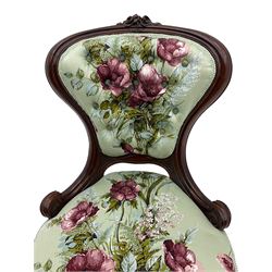 Victorian walnut framed nursing chair, spade shaped back carved with flower heads, upholstered in buttoned rose patterned fabric, on scroll carved cabriole supports terminating at brass and ceramic castors