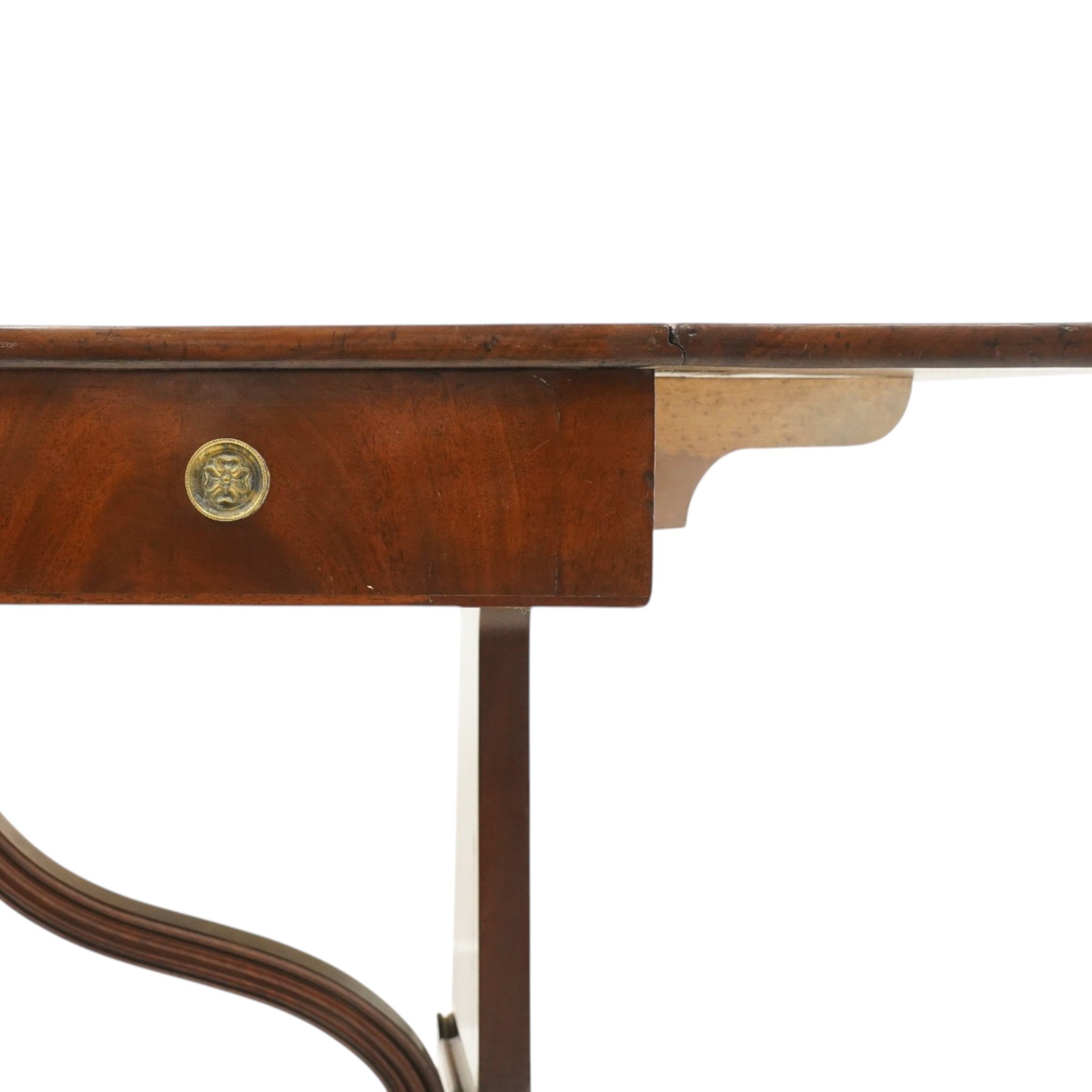 Early 20th century Regency Revival figured mahogany sofa table, rectangular drop-leaf top with rounded corners, fitted with two drawers to each side with brass flowerhead pull handles, raised on twin end supports with splayed reeded legs and brass cups and castors, united by a scrolling and reeded closed stretcher