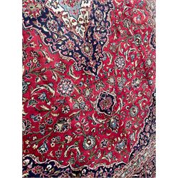 Central Persian Kashan crimson ground carpet, central  floral pole medallion with matching spandrels within a field of scrolling palmette motifs and foliage, the heavily banded indigo border with repeating plant motifs interlaced with scrolled branches