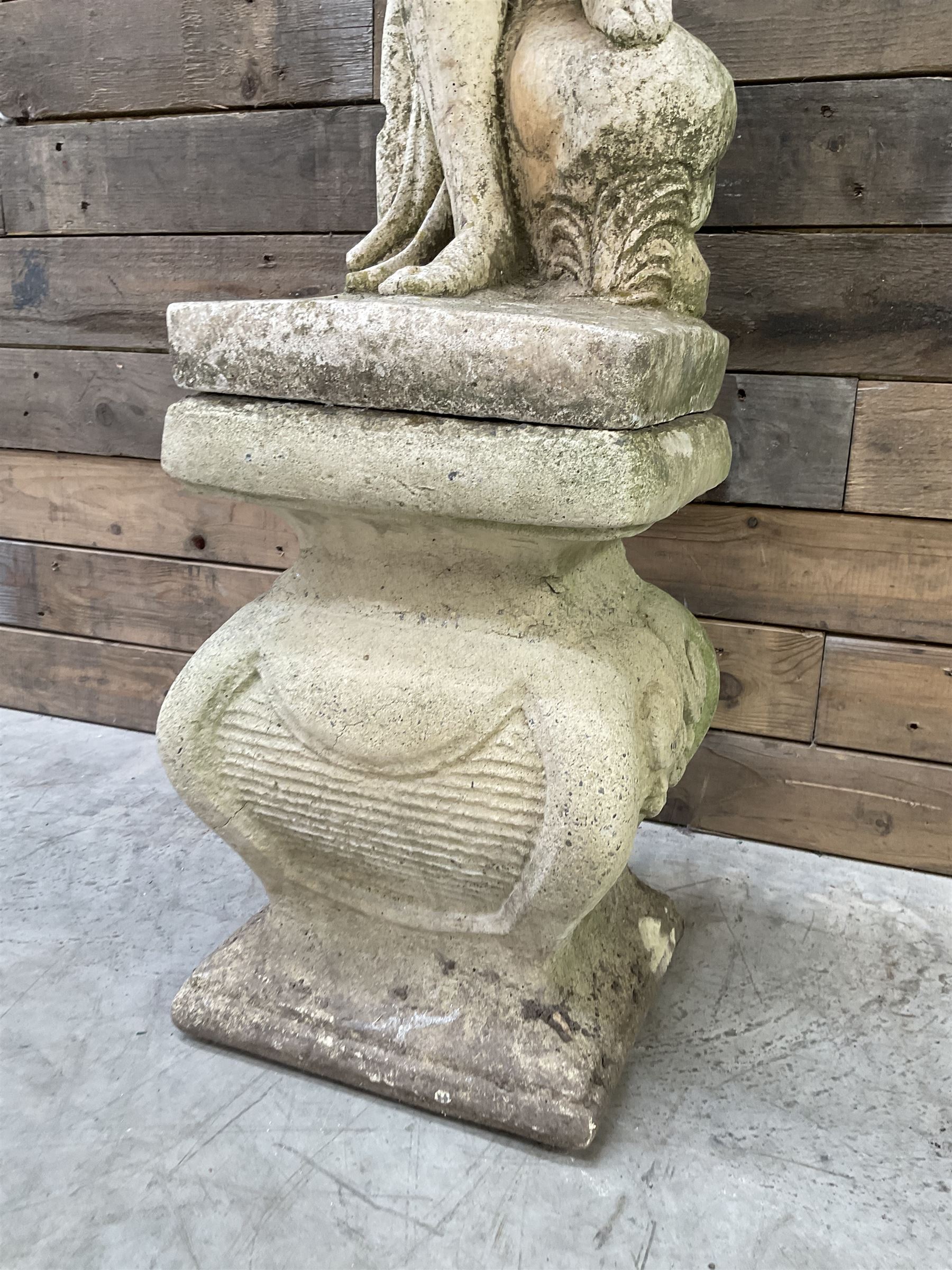 Cast stone garden statue of partially draped classical female figure on ornate pedestal 