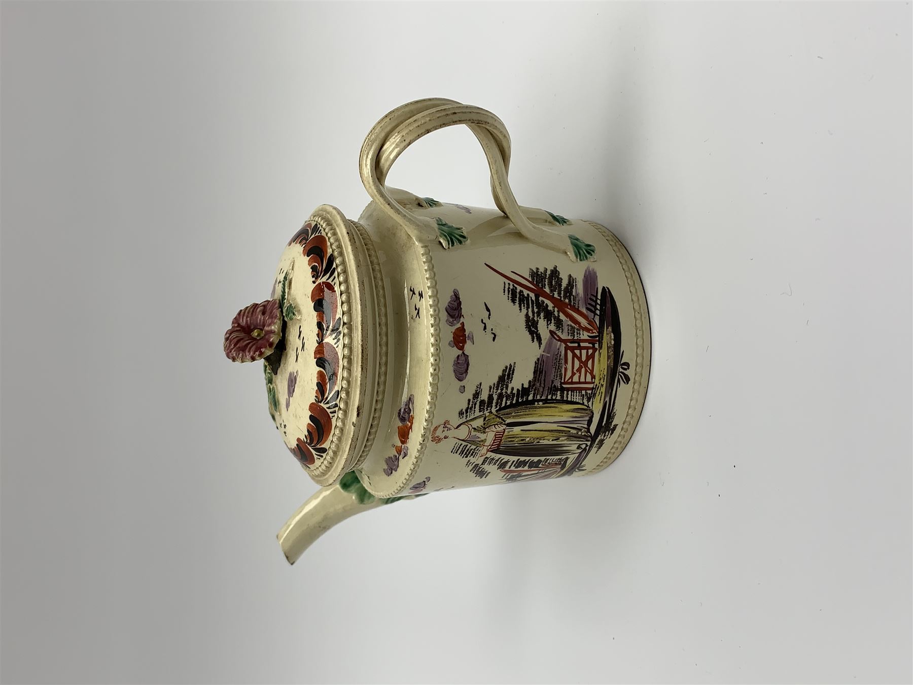 18th century creamware teapot, probably Leeds, with reeded entwined handle and floral finial to the cover, the body with hand painted polychrome decoration of figure to one side, and floral spray to the other, collectors paper label beneath inscribed Leeds Pottery, H11.5cm