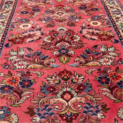 Persian rose ground runner rug, the field decorated with repeating polychrome floral sprays and scrolling palmettes, enclosed by an ivory floral border and narrow navy geometric guard stripes