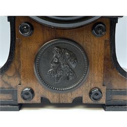 Compact mahogany veneered library clock c1890, with ebonised mouldings and applied raised cross banding, Parisian eight-day timepiece movement housed in a drum case resting on a shaped plinth with a circular portrait relief of classical antiquity to the front,  3-1/2” enamel dial and steel  moon hands, Roman numerals and minute markers, plain spun bezel with a flat bevelled glass. With pendulum.


