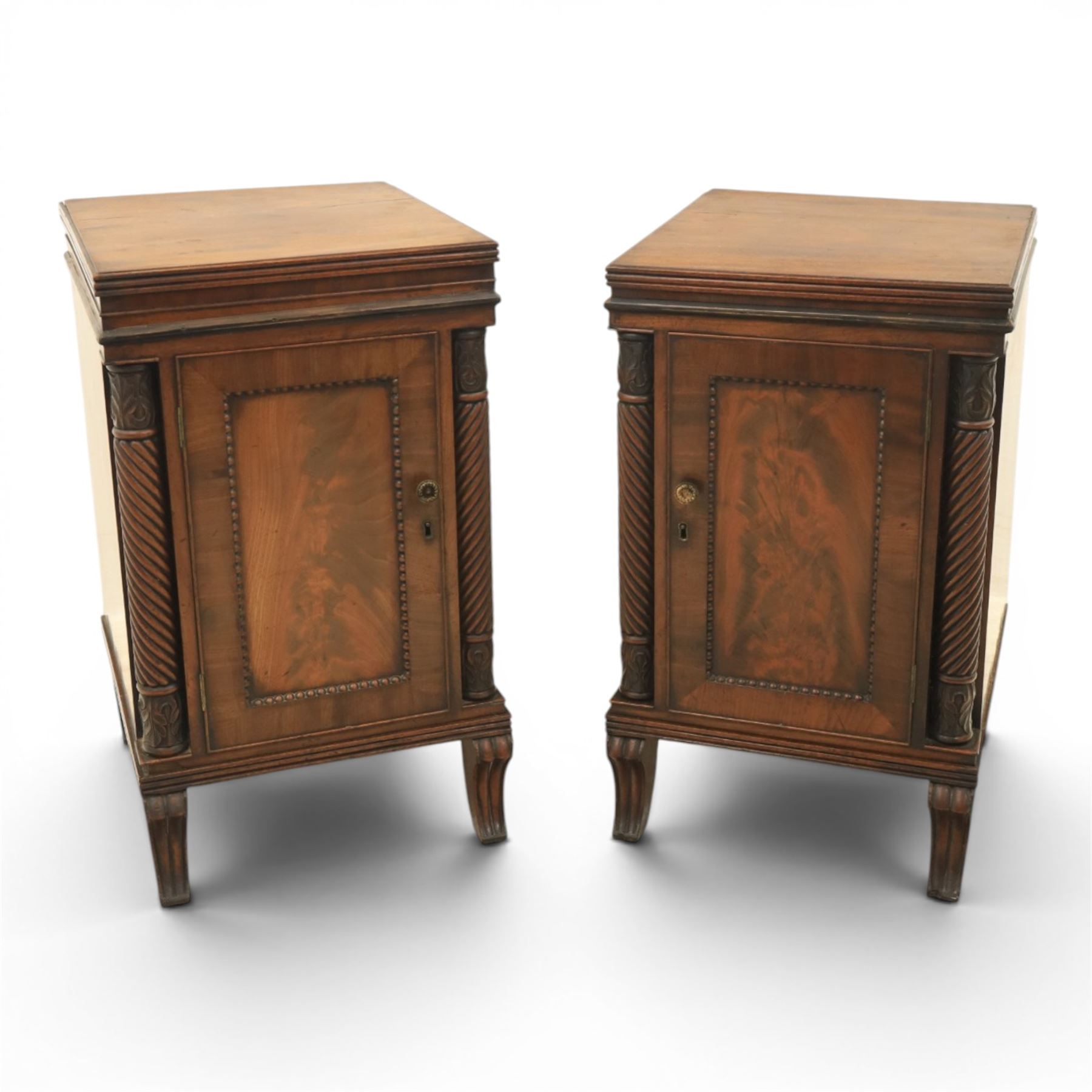  Pair of Regency mahogany bedside cabinets, rectangular top above a central cupboard door with flame mahogany veneer, flanked by spirally turned column uprights, raised on shaped supports