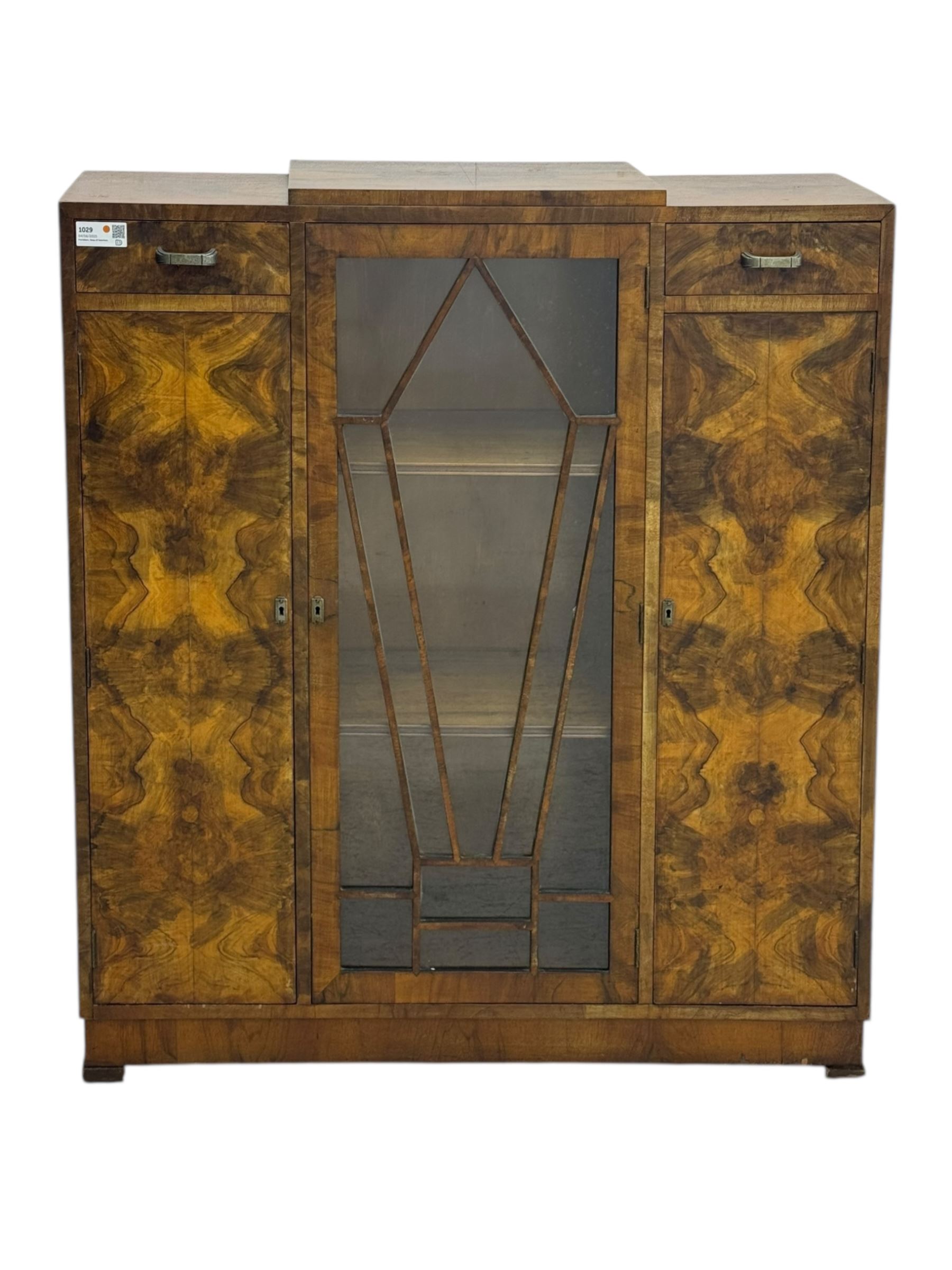Art Deco burr walnut drinks cabinet, geometric central glazed astragal door enclosing two fixed shelves, flanked by symmetrical bookmatched veneered cupboards with drawers above 
