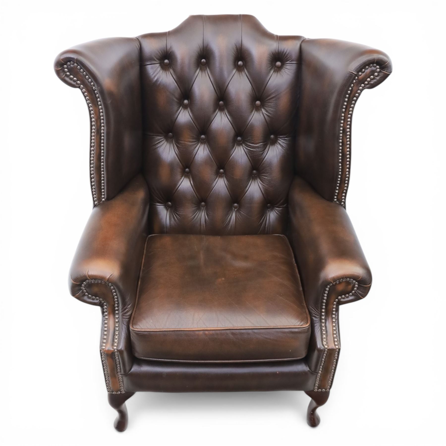 20th century Chesterfield style brown leather wingback armchairs, with button upholstered backs and wings, shaped scroll arms with studded borders, loose seat cushions, raised on cabriole supports with pad feet