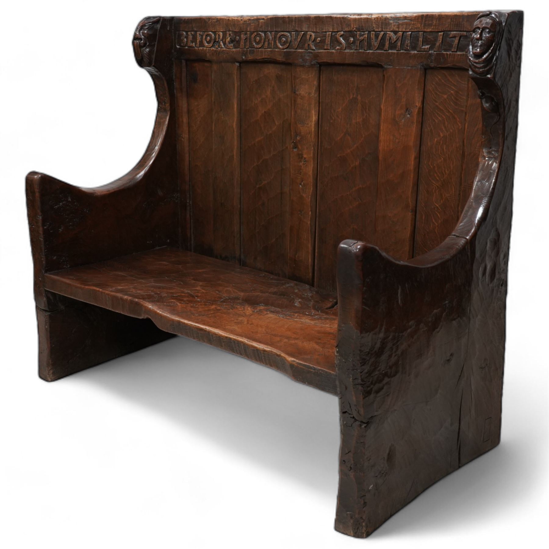 Mouseman - circa. 1920s adzed oak settle or bench, the cresting rail carved with inscription 'Before Honour is Humility', four panel back and plank seat on shaped end supports carved with grotesque masks terminals, carved with mouse signature, by Robert Thompson of Kilburn 

