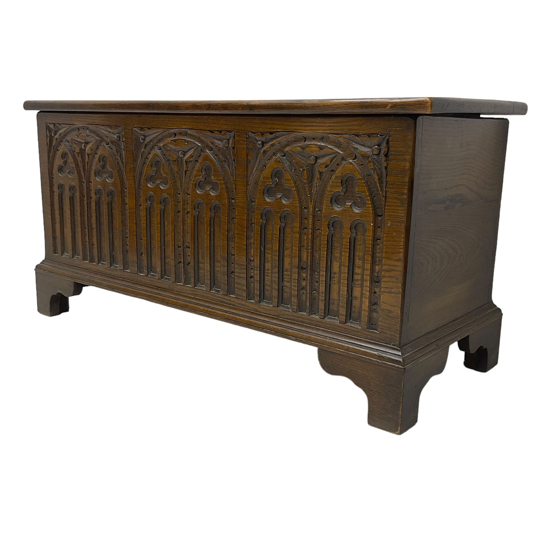 Mid-20th century oak blanket box, hinged lid over front carved with Gothic tracery work and flower heads, on bracket feet
