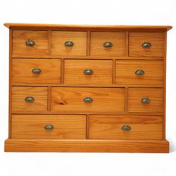 Late 20th century pine merchants chest, rectangular top over an arrangement of twelve small and four larger drawers, each with recessed panel facias and brass cup handles, plinth base