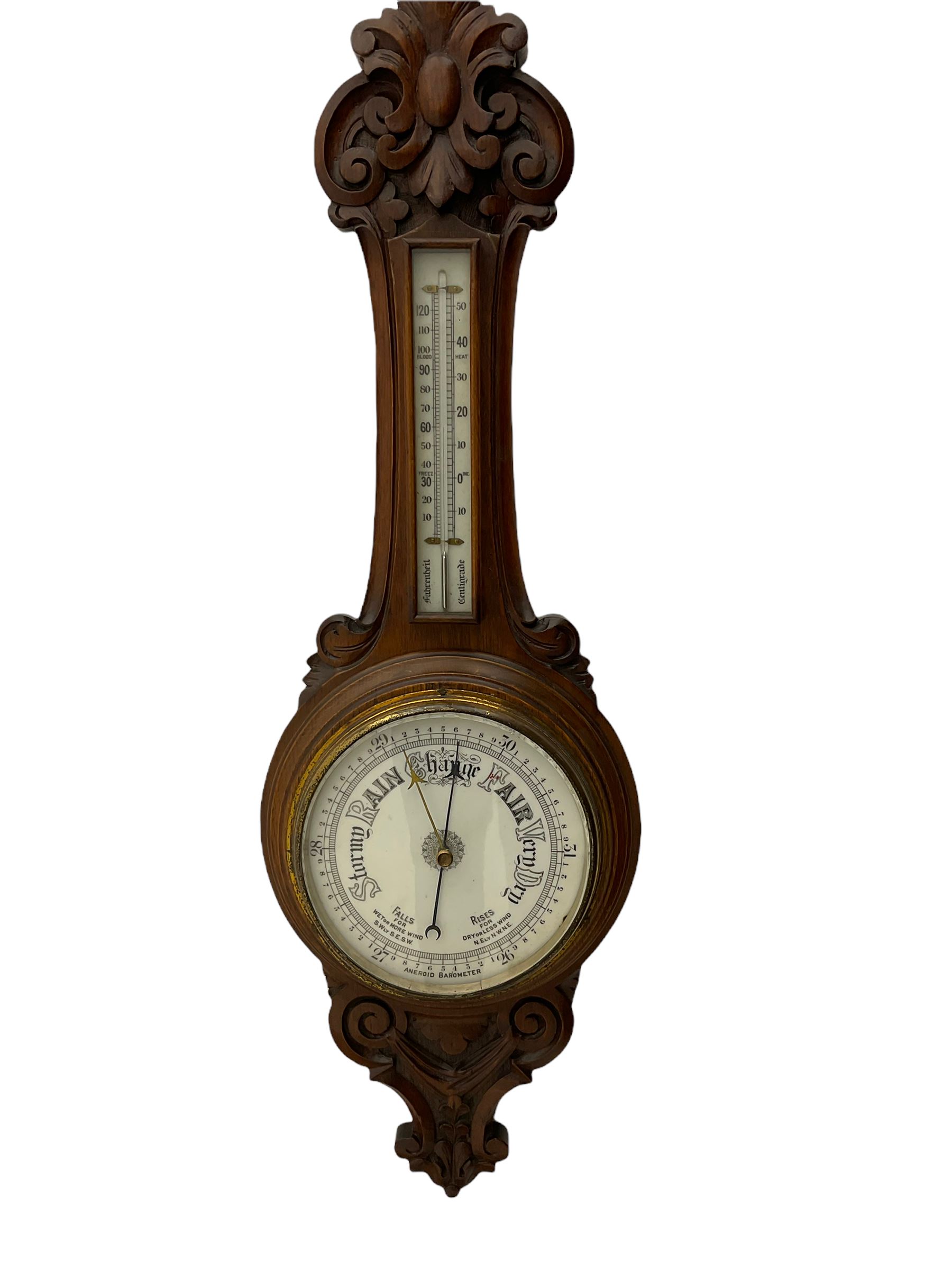 An English 1930’s solid oak carved hall barometer in a scroll shaped carved case with relief carving, aneroid movement, 8” white register measuring barometric air pressure from twenty-six to thirty-one point nine inches, weather predictions in black upper and lower case gothic script with a blue steel indicating hand and brass recording hand, brass dial bezel with flat bevelled glass, mercury thermometer enclosed in a glazed rectangular box displaying temperature in degrees Fahrenheit and Celsius on a white register. H87cm


