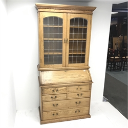 Early 20th Century light oak bureau bookcase, two lead glazed doors, three adjustable shelves above fall front enclosing fitted interior, four short and two long drawers, platform base, W101cm, H213cm, D54cm