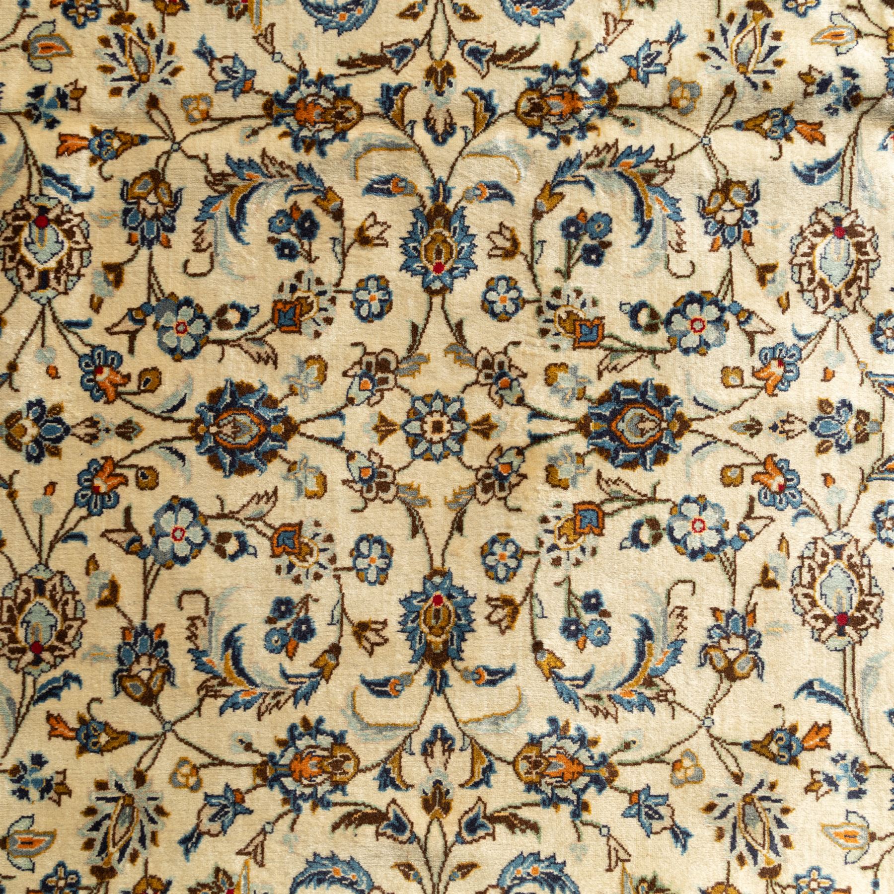 Central Persian Kashan rug, cream ground densely patterned with interlaced floral stems and rosettes in blue, gold and brown, framed by layered borders featuring stylised palmettes, woven in the Kashan weaving district of Iran