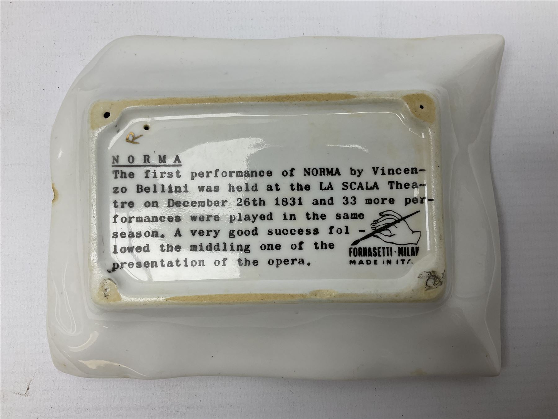 Two Fornasetti rectangular operatic posters ashtrays 'Norma' and 'Iris' decorated with black and white text with a gilt border edge, with printed mark beneath, H16cm