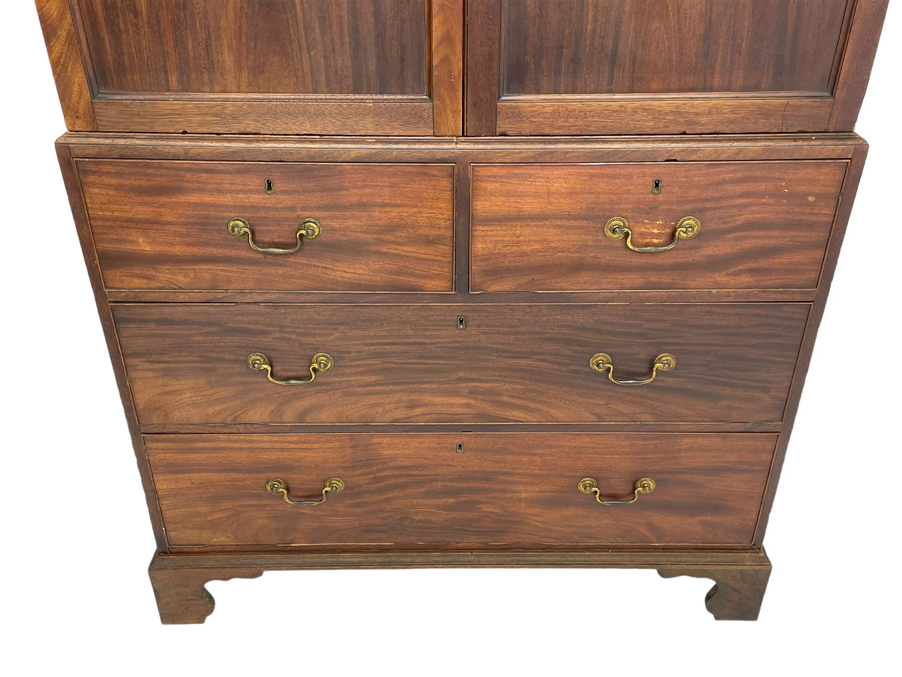 George III mahogany Gentleman's linen press, the projecting cornice over two panelled cupboard doors enclosing three sliding trays, the base fitted with two short over three long graduating cock-beaded drawers, lower moulded edge over bracket feet