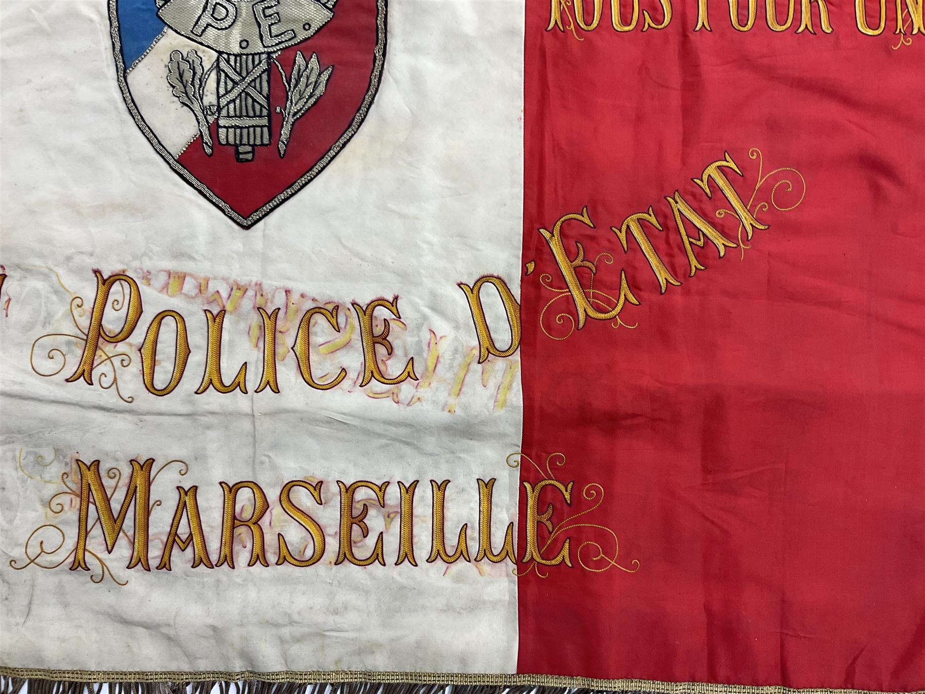 French State Police banner as the tricolor flag embroidered with coloured and metallic thread 'Societe De Secours Mutuels Un Pour Tous Tous Pour Un De La Police D'Eteat De Marseille' to one side; plain flag verso; tassels to three sides 100 x 113cm